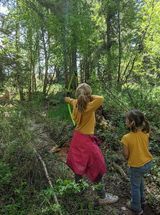 Two young girls are playing with bows and arrows in the woods.