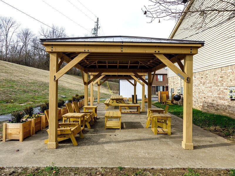 Wooden gazebo with seating on a concrete patio. Planter boxes line one side, hillside in background at Glastonbury Woods Apartments.