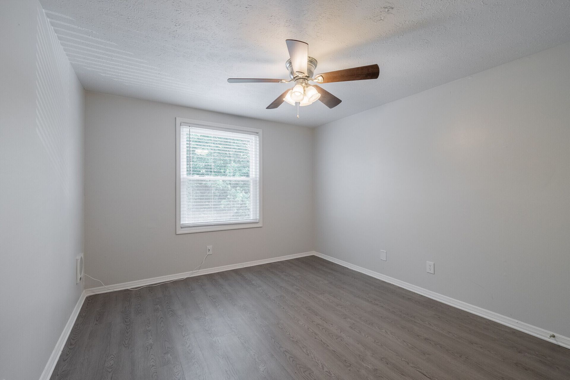 Empty bedroom with gray walls, wood-look floor, window, ceiling fan at Glastonbury Woods Apartments.