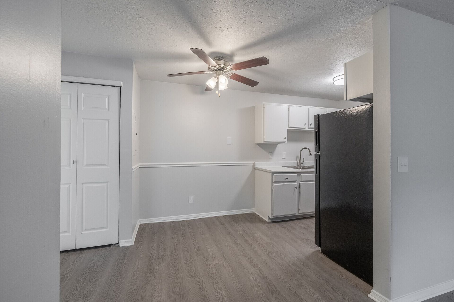 Interior view of a kitchen and dining area with white cabinets, gray walls, and dark flooring; black refrigerator at Glastonbury Woods Apartments.