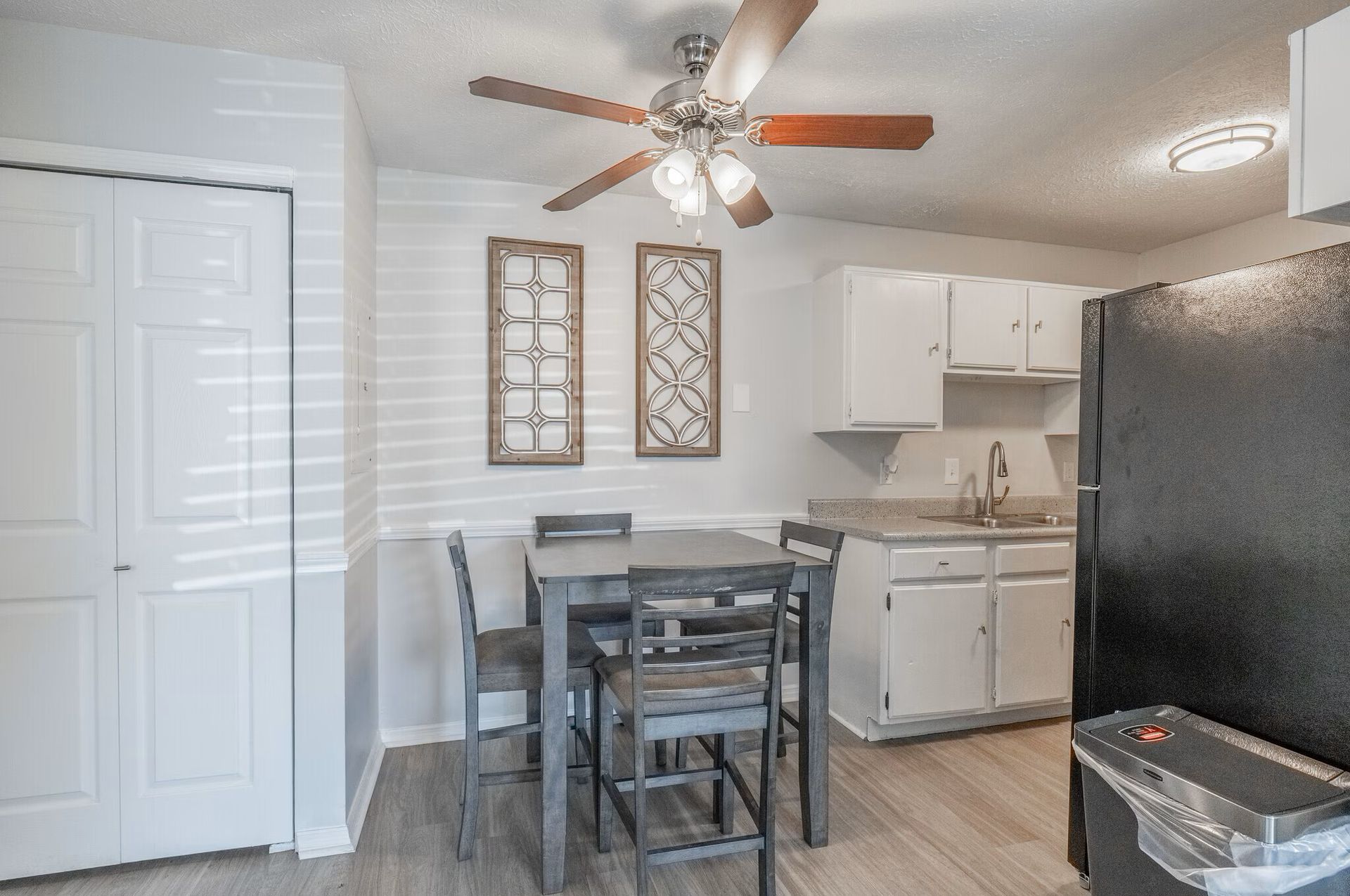 A small kitchen at Glastonbury Woods Apartments with a dining table, white cabinets, and a black refrigerator.