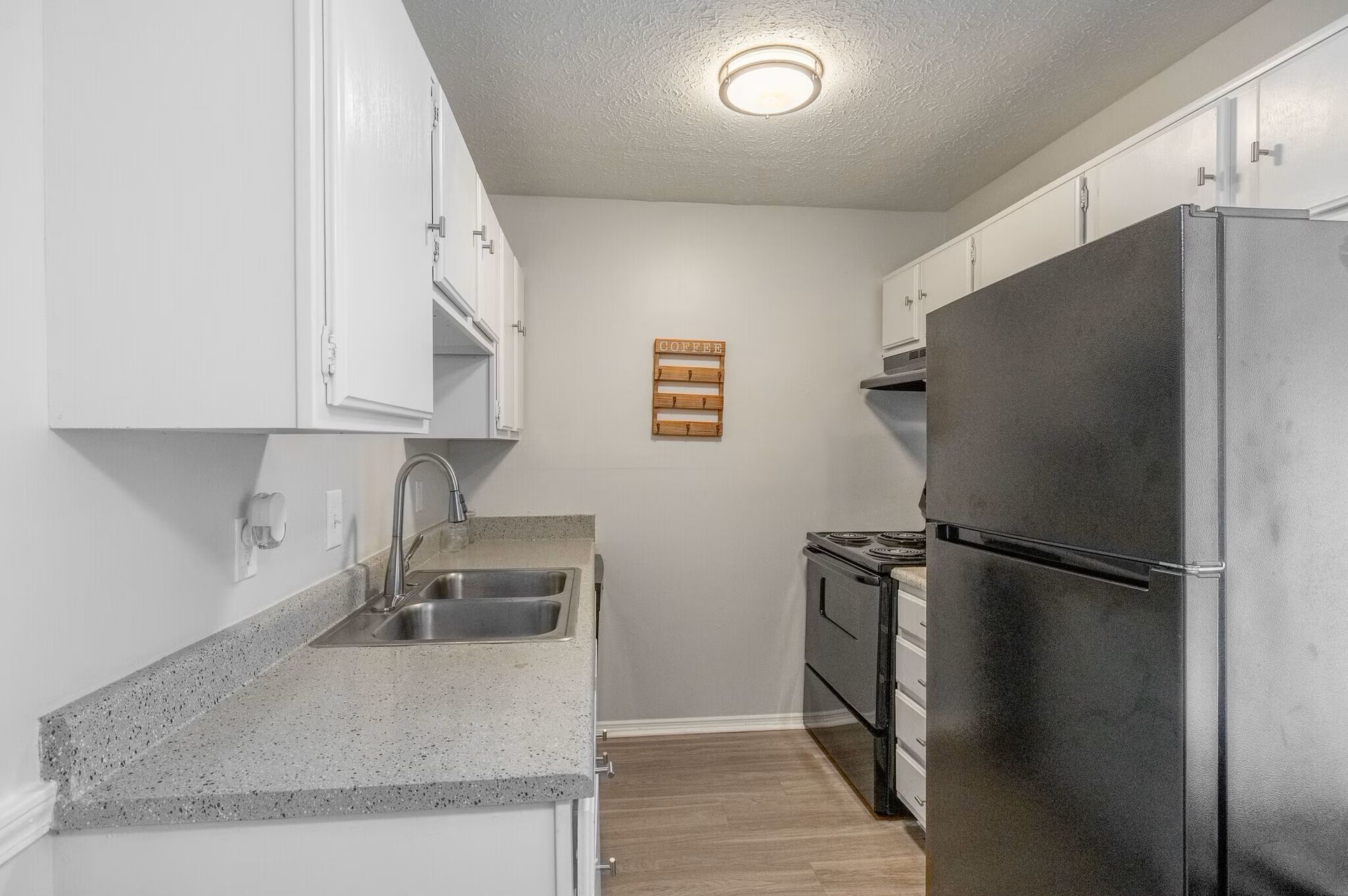 Glastonbury Woods Apartments Kitchen with white cabinets, light gray countertops, black appliances, and wooden floors.