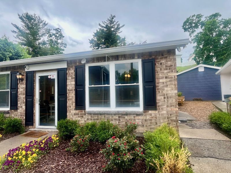 Brick house with black shutters, white-framed window, and a door, with landscaping in front at Glastonbury Woods Apartments.