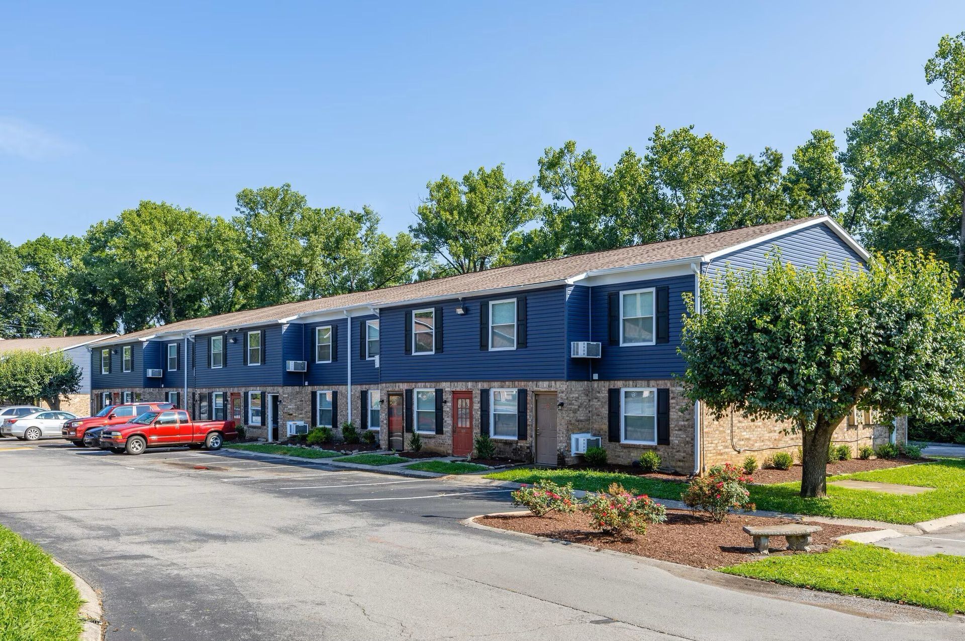 Blue two-story apartment building at Glastonbury Woods Apartments with black shutters and a red car parked out front.
