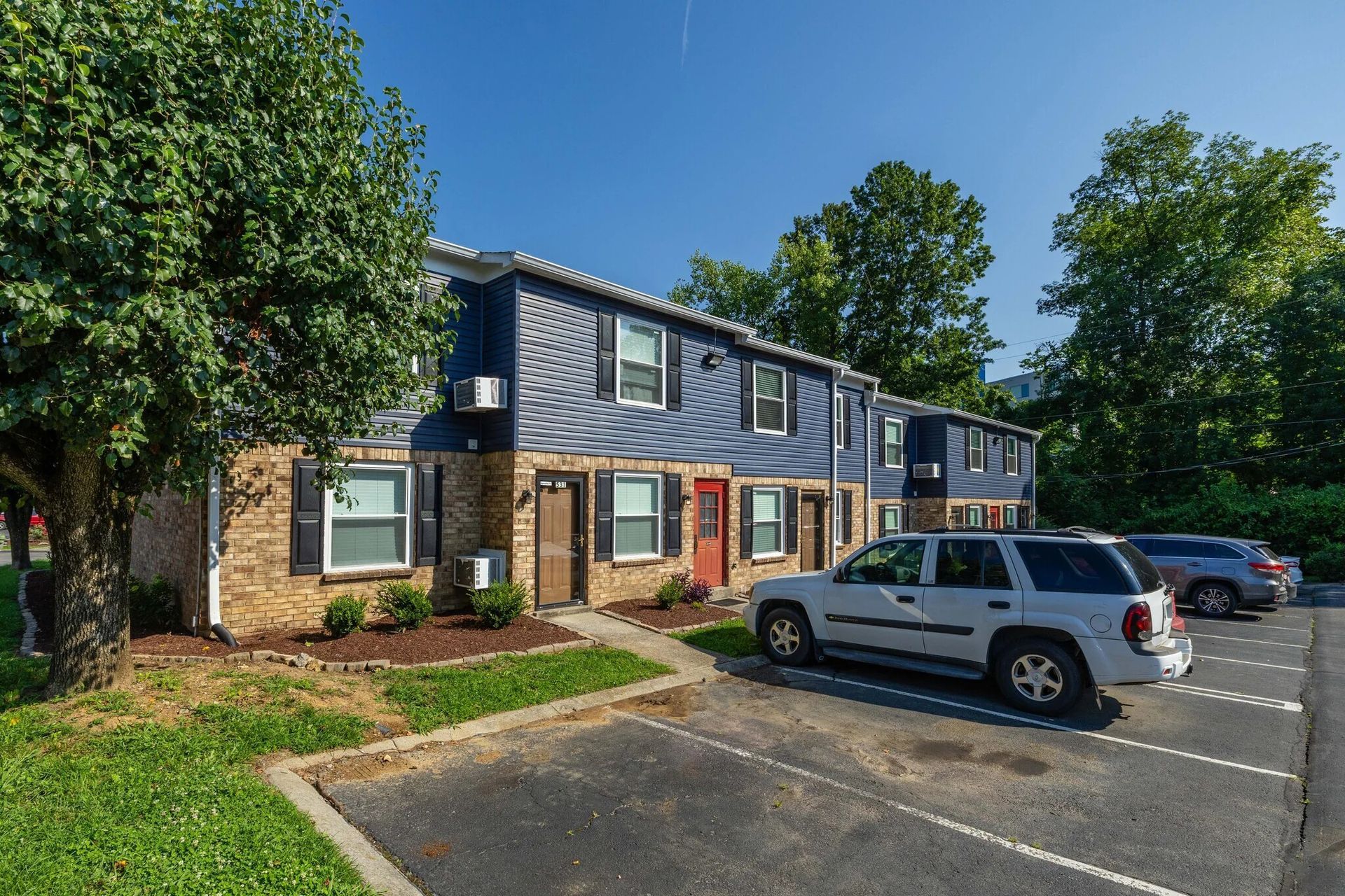 Blue and brick apartment building with parking, a silver SUV is parked in front at Glastonbury Woods Apartments.