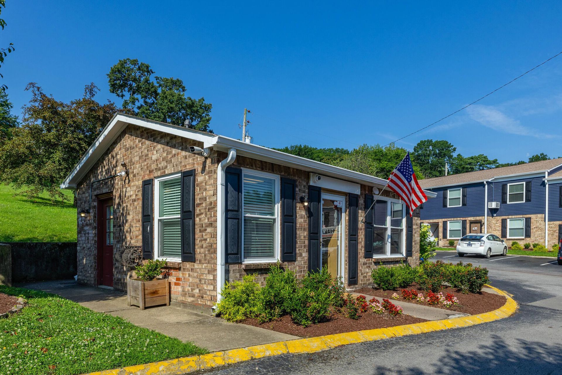 Glastonbury Woods Apartments building with American flag, black shutters, and landscaping, sunny day.