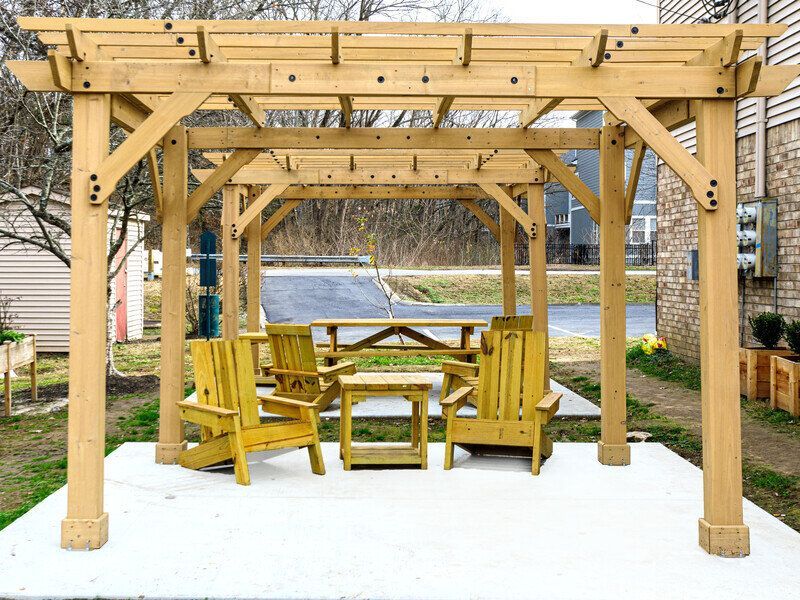 Wooden pergola over patio with seating: Adirondack chairs, small table, picnic table at Glastonbury Woods Apartments.