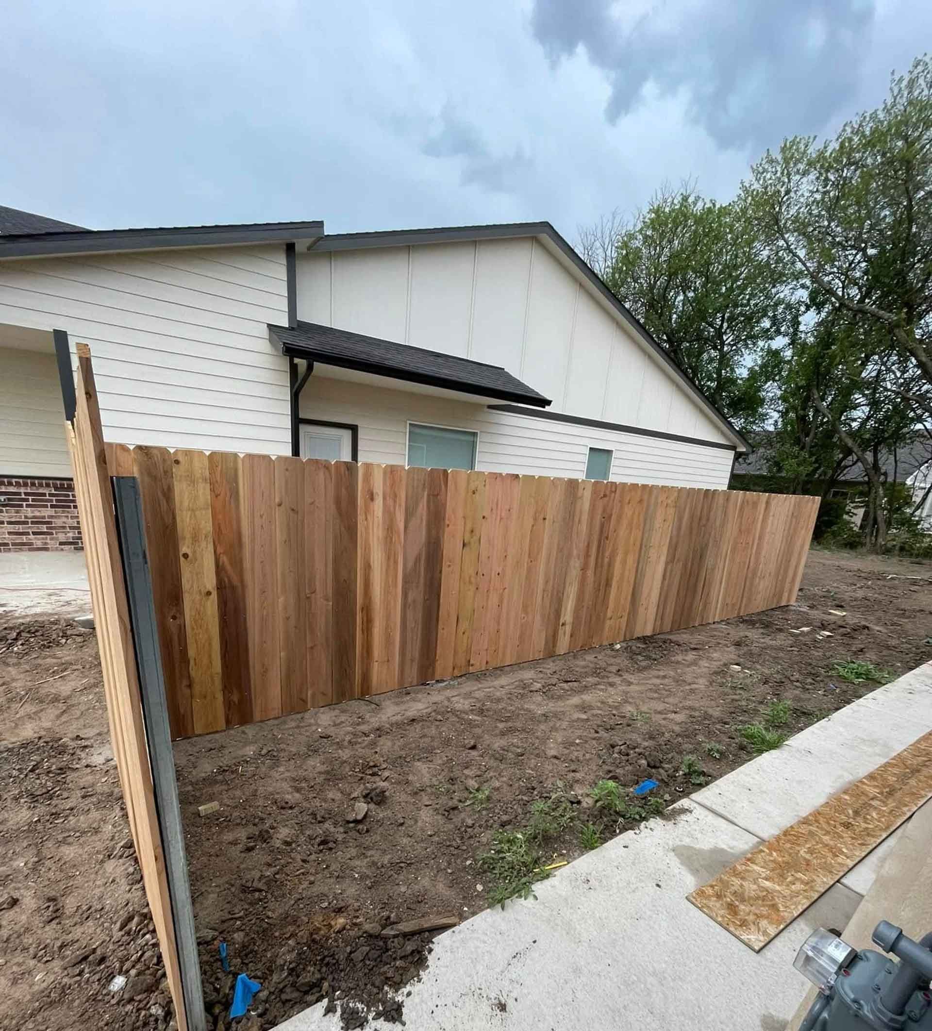 Wooden fence partially constructed next to a house on a cloudy day.