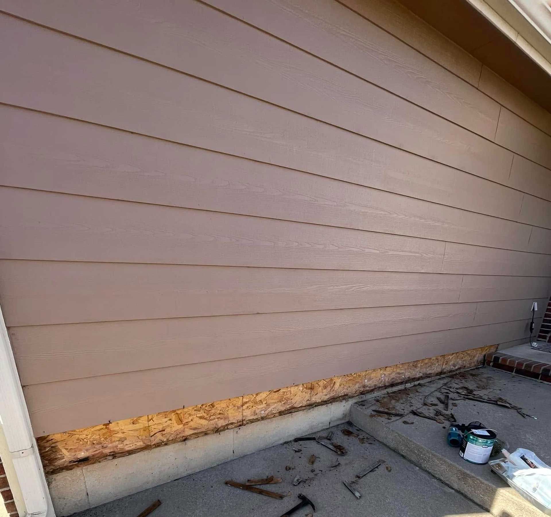 Exterior wall with missing siding, exposing wood framing near a concrete slab.