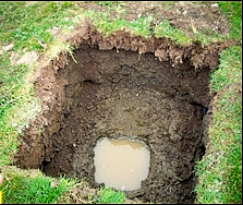 Surveying tools around a freshly dug hole in a grassy yard, with a shovel and level nearby.