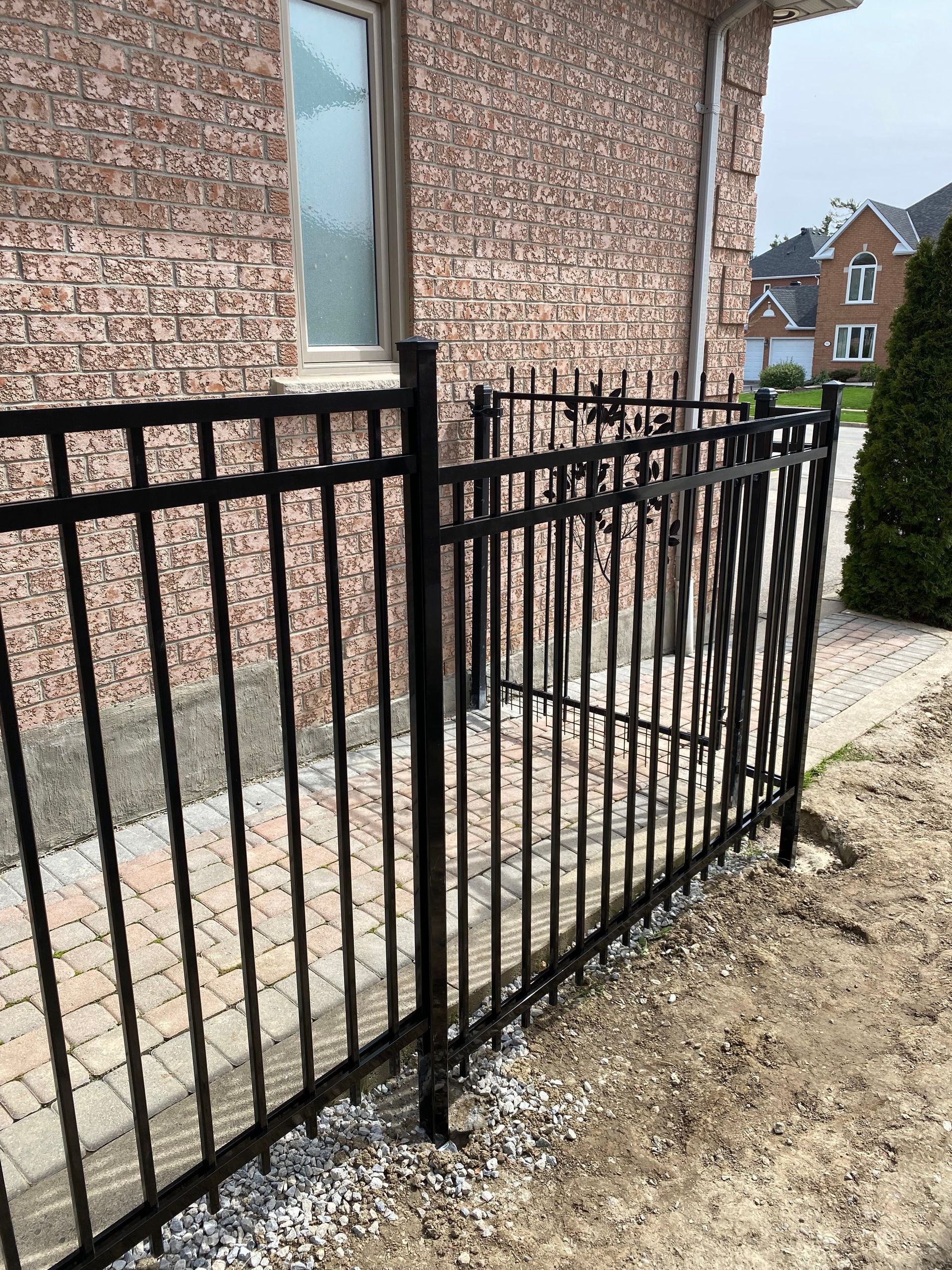 A black metal fence is sitting in front of a brick house.