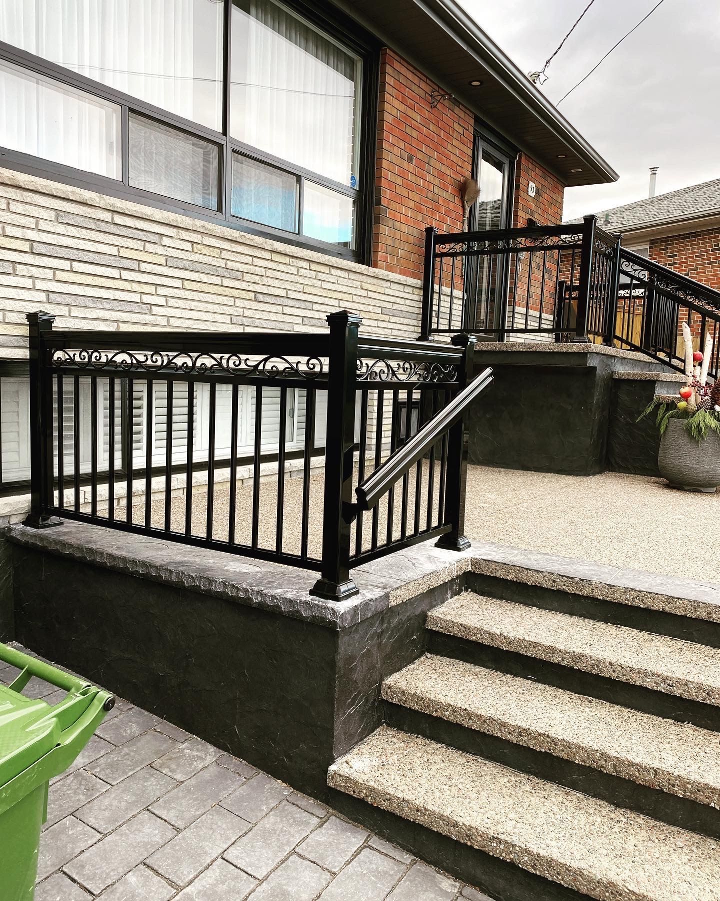 A brick house with a black railing and stairs leading up to it.