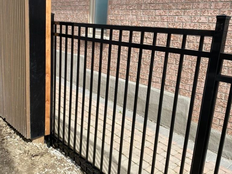 A black metal fence surrounds a lush green yard in front of a house.