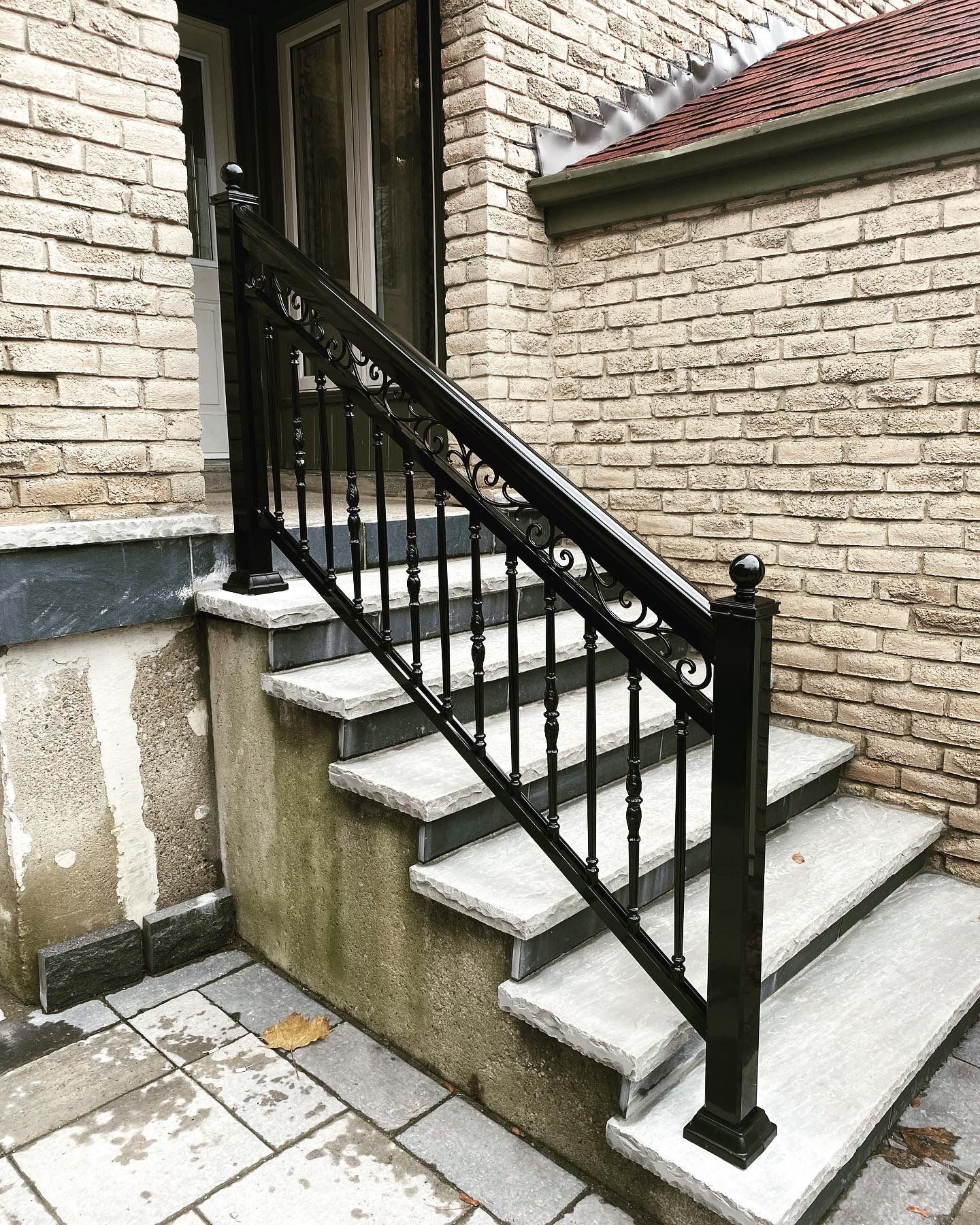 A set of stairs with a black railing in front of a brick building.
