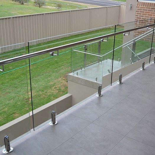 A balcony with a glass railing and a fence in the background.