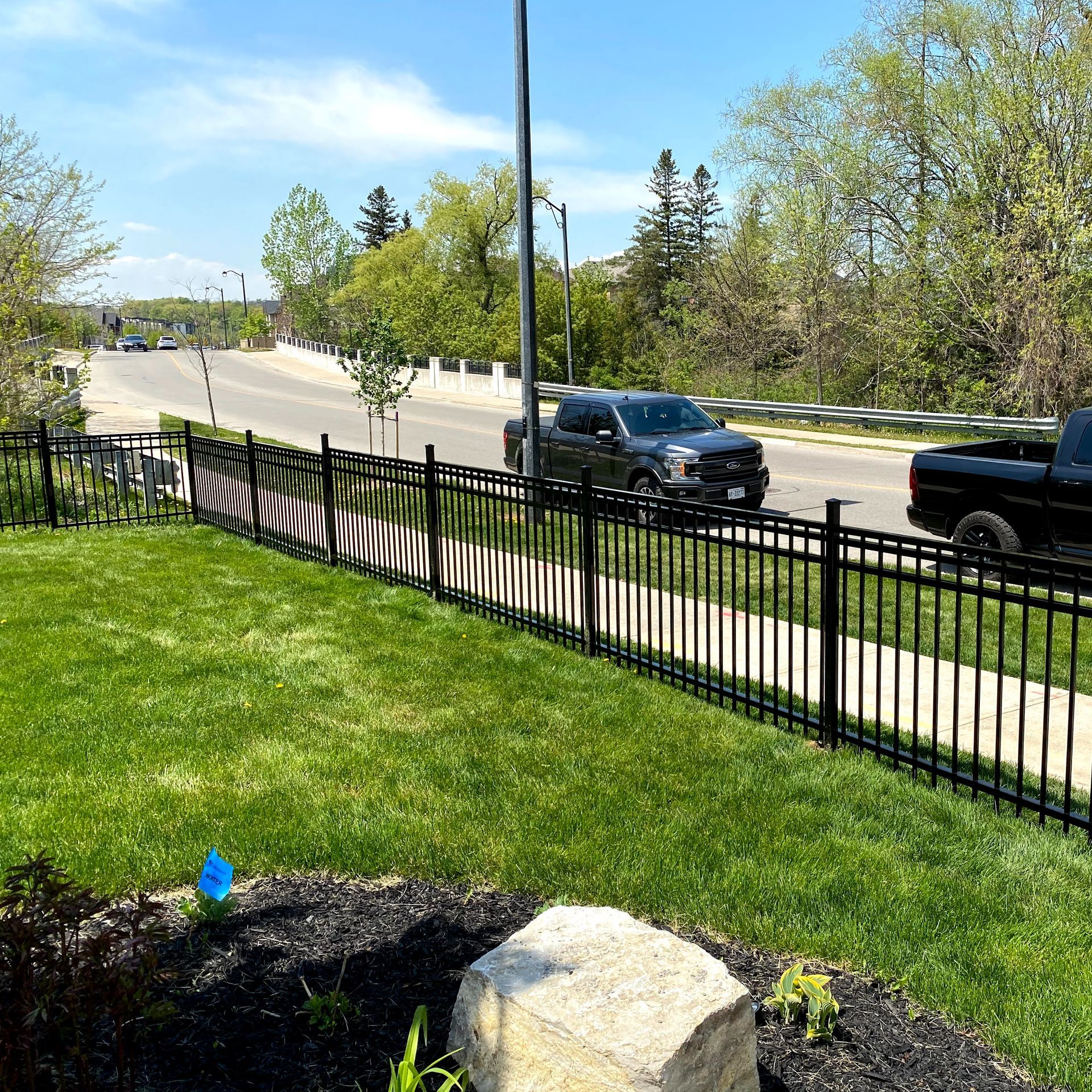 A black truck is parked on the side of the road behind a fence