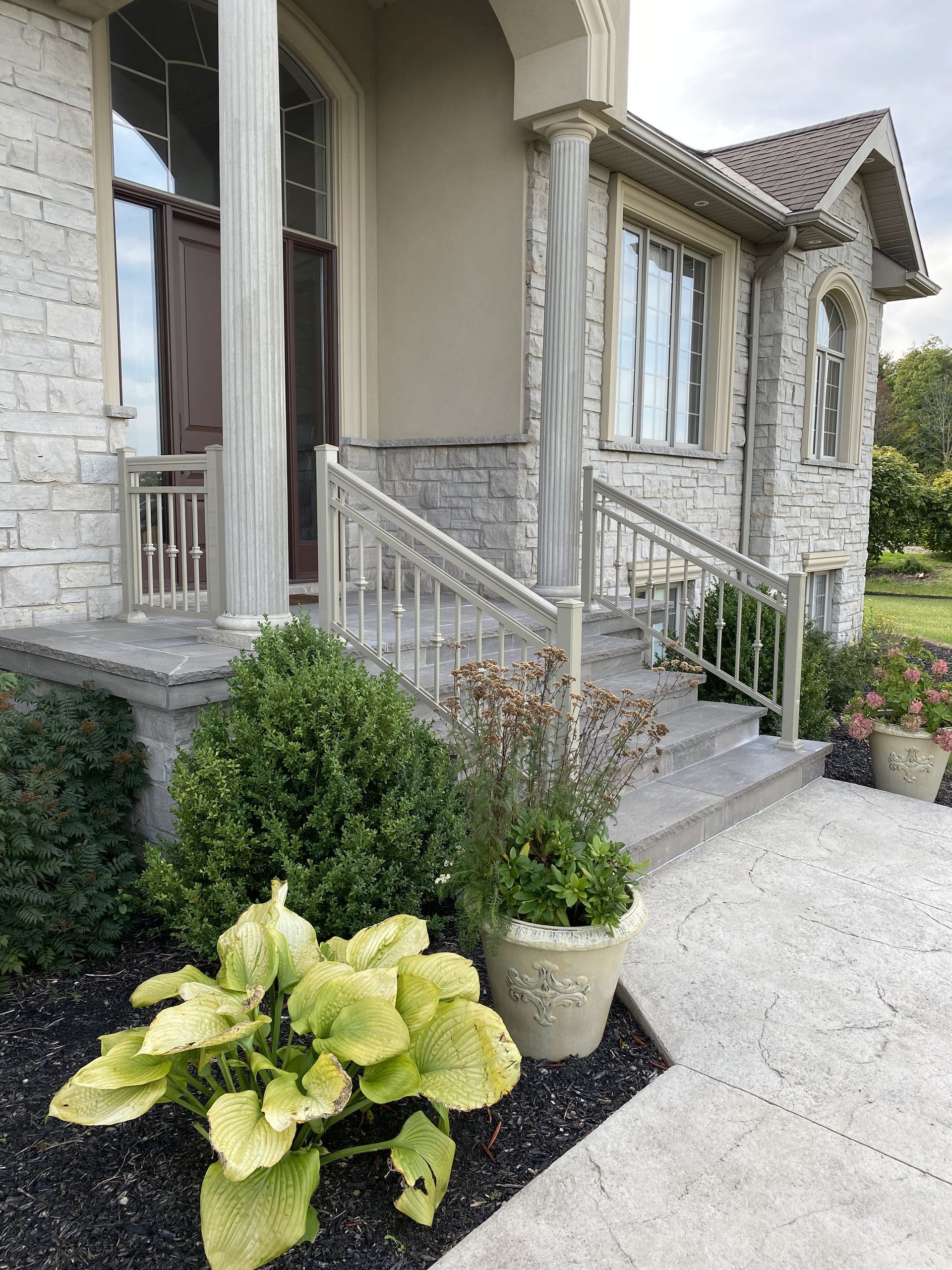 A house with a porch and stairs and plants in front of it.
