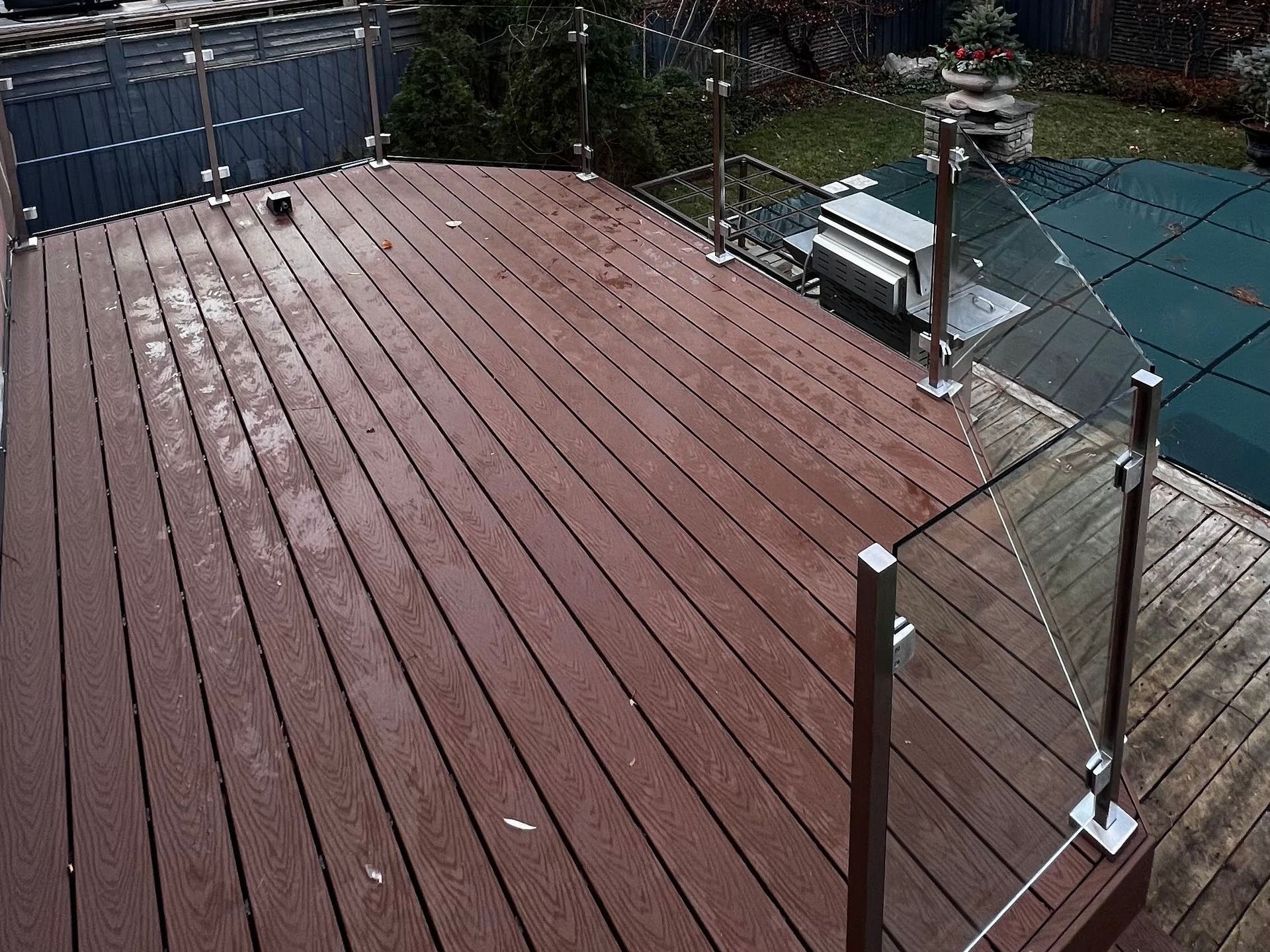 A wooden deck with a glass railing next to a pool