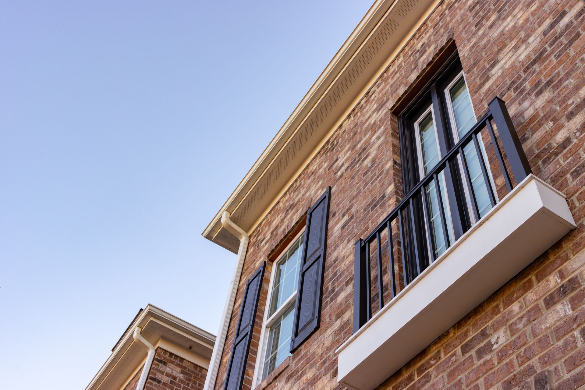 A brick building with a balcony and shutters on the windows.