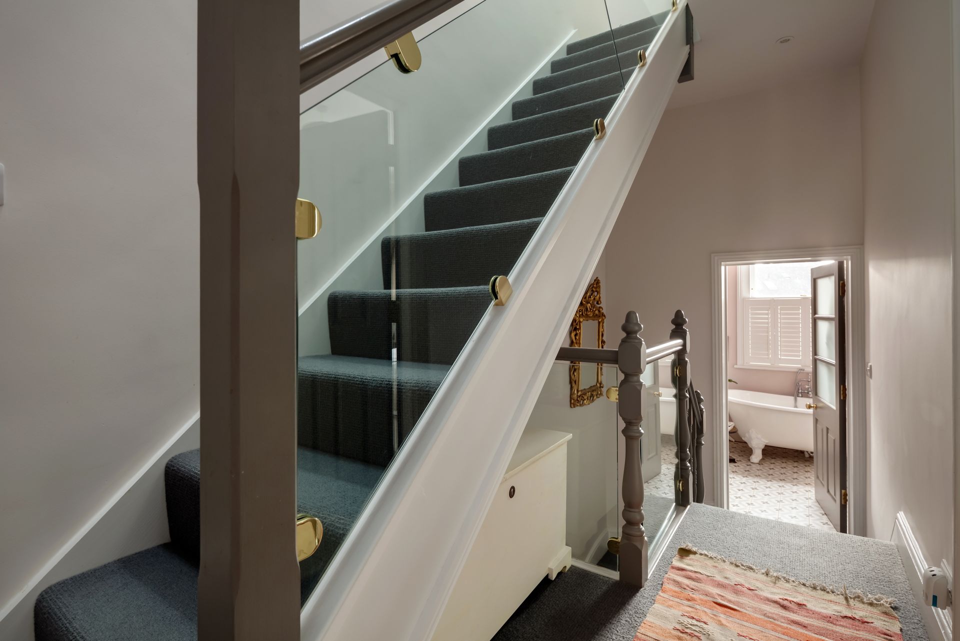 A staircase with a glass railing in a hallway leading to a bathroom.