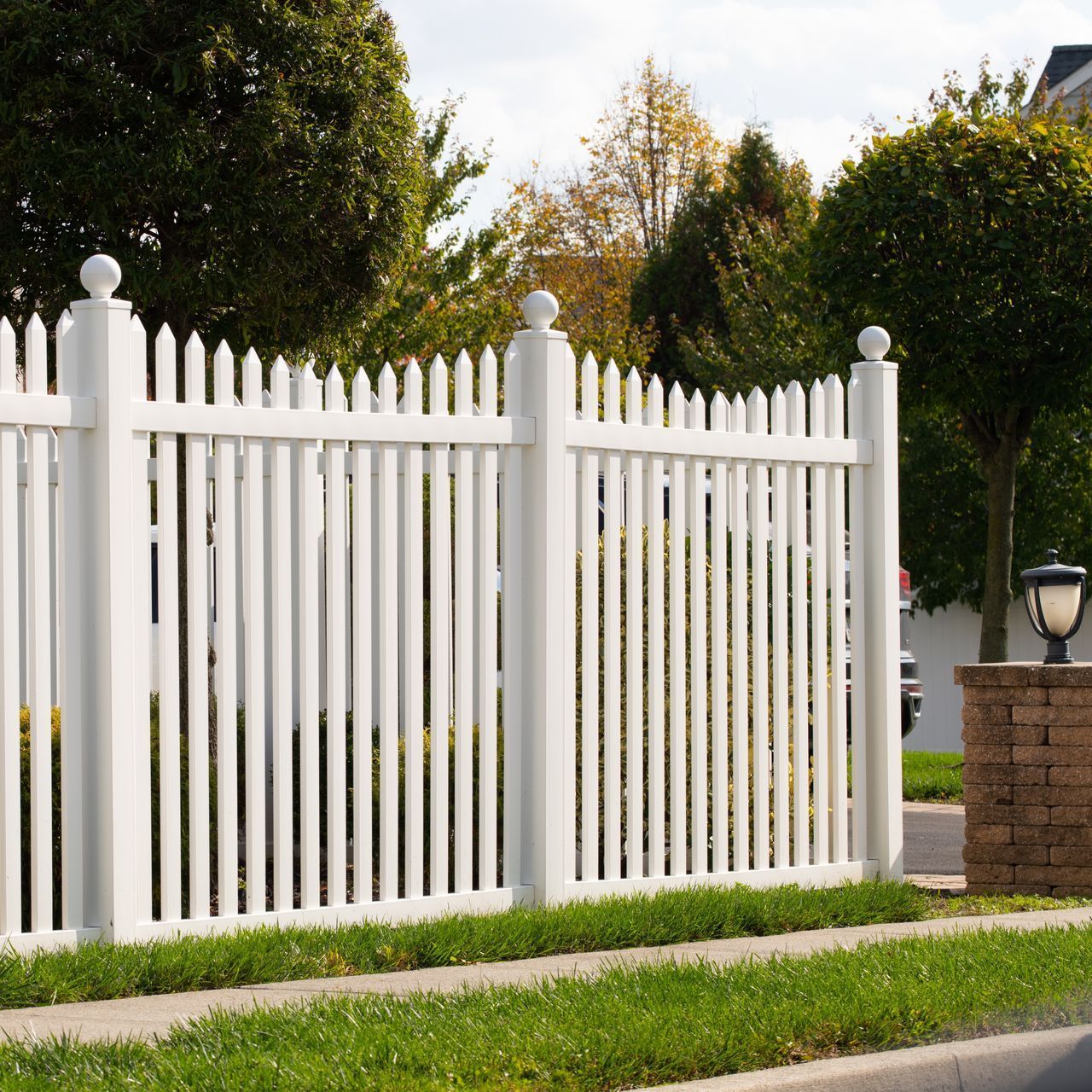 A white picket fence is surrounded by grass and trees
