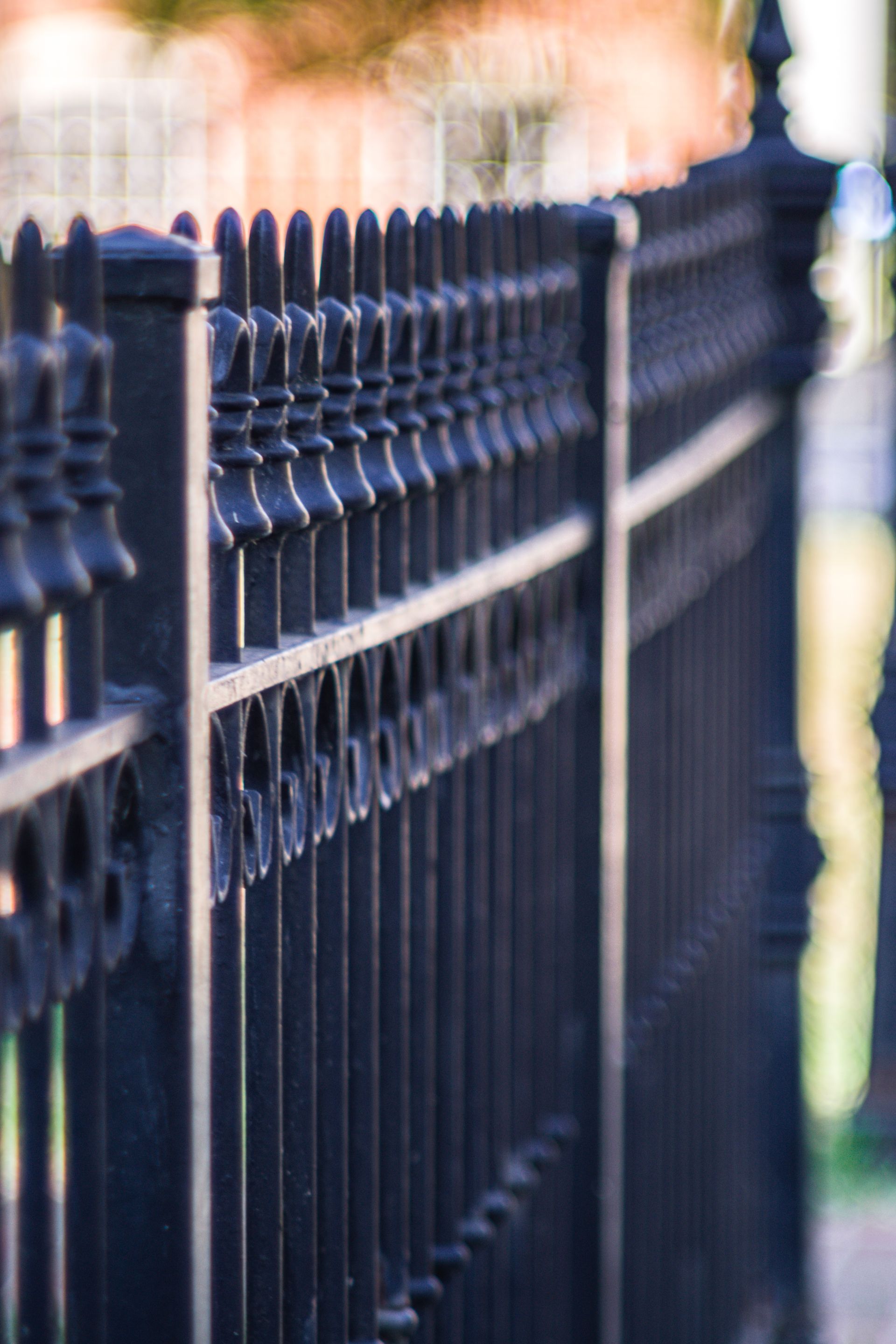 A close up of a black wrought iron fence with a blurred background.