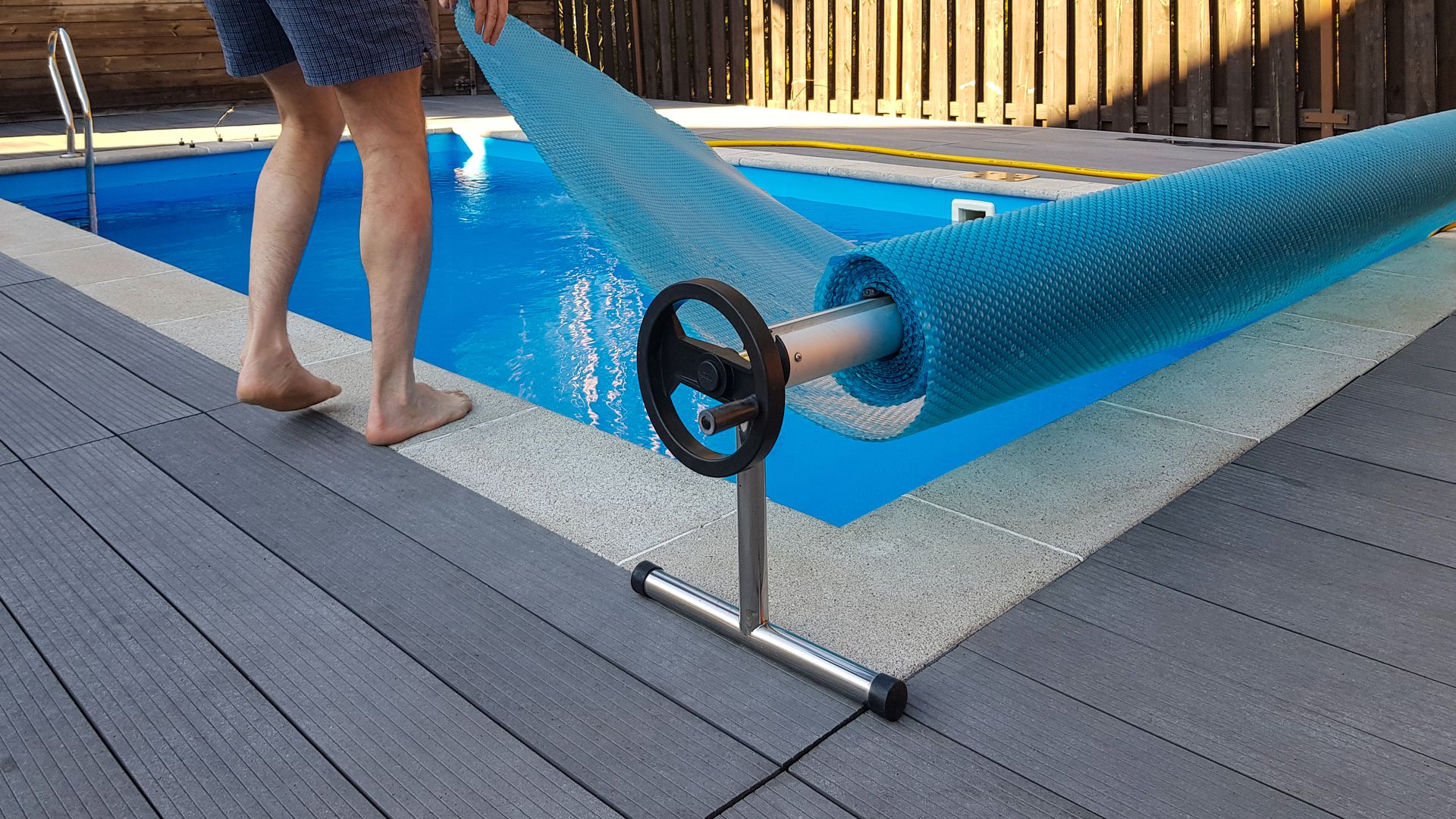 A person is standing on a deck next to a swimming pool.