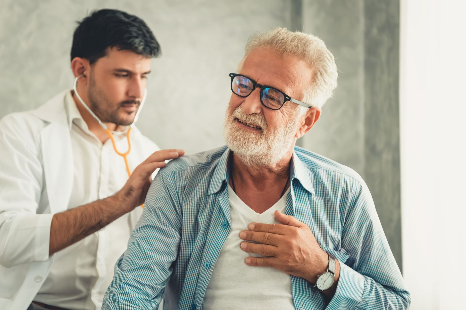 A doctor is examining an older man 's heart with a stethoscope.