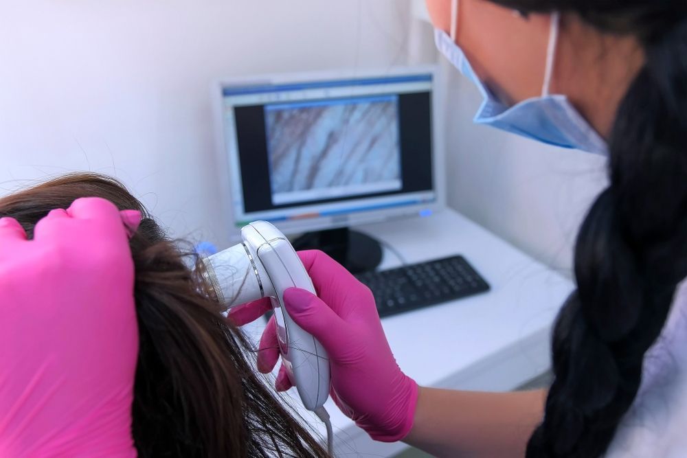 A woman in pink gloves is examining a woman 's hair.