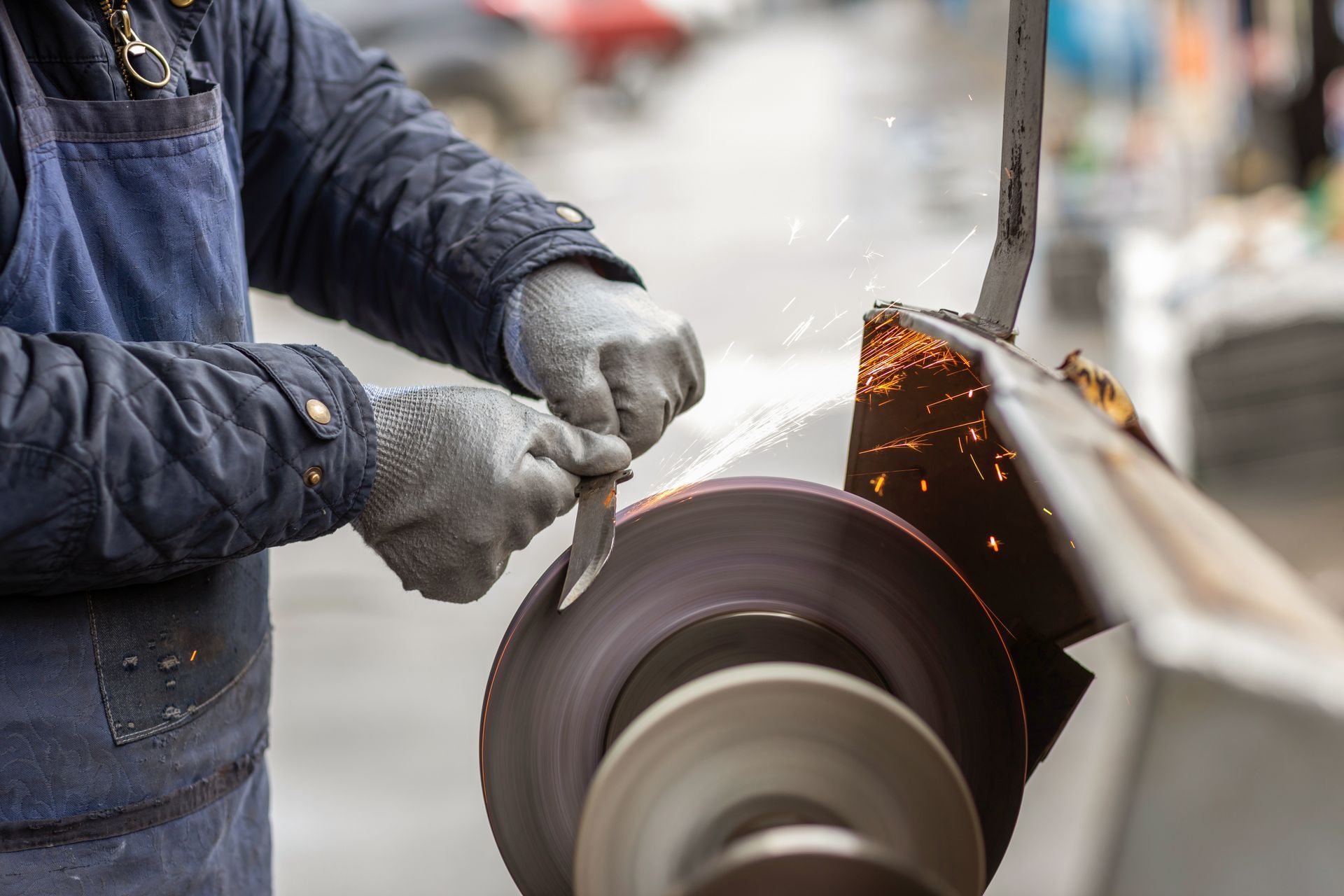 Hands sharpening a blade on a grinding wheel, with bright sparks flying in a workshop.