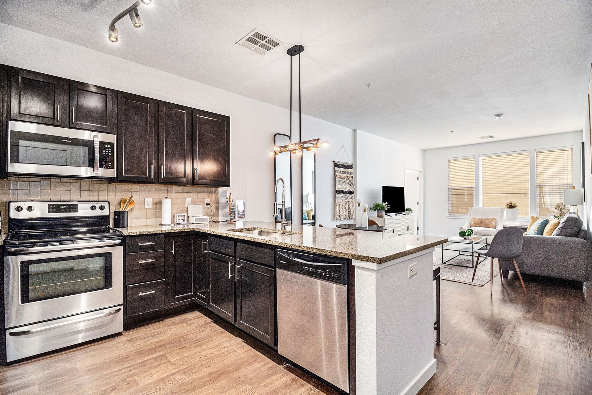 Modern kitchen with dark cabinets, stainless appliances, island, and view into a bright living room