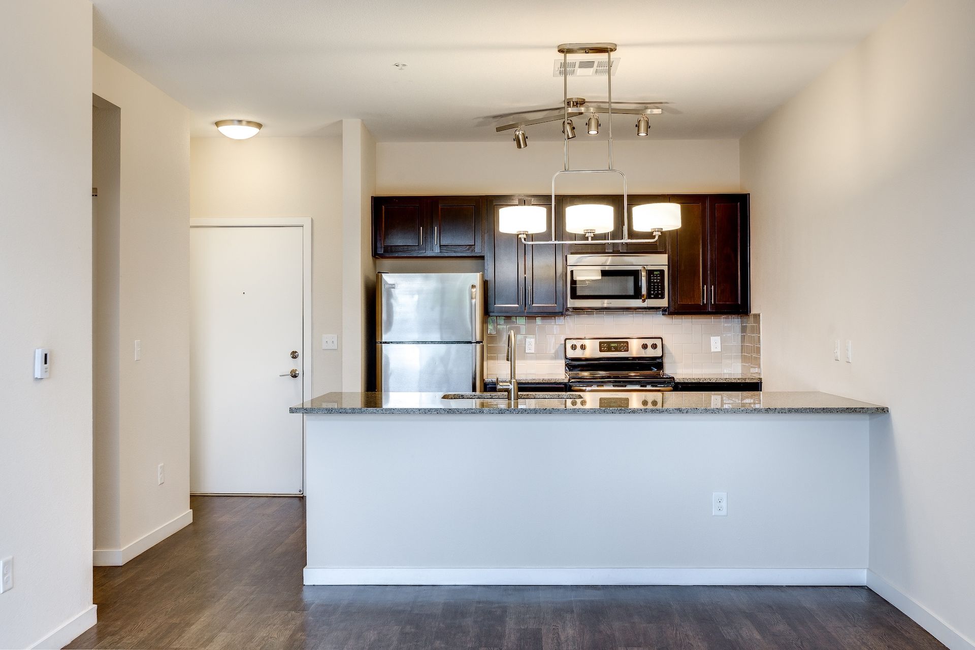 Modern apartment kitchen with dark cabinets, stainless appliances, granite counter, and breakfast bar