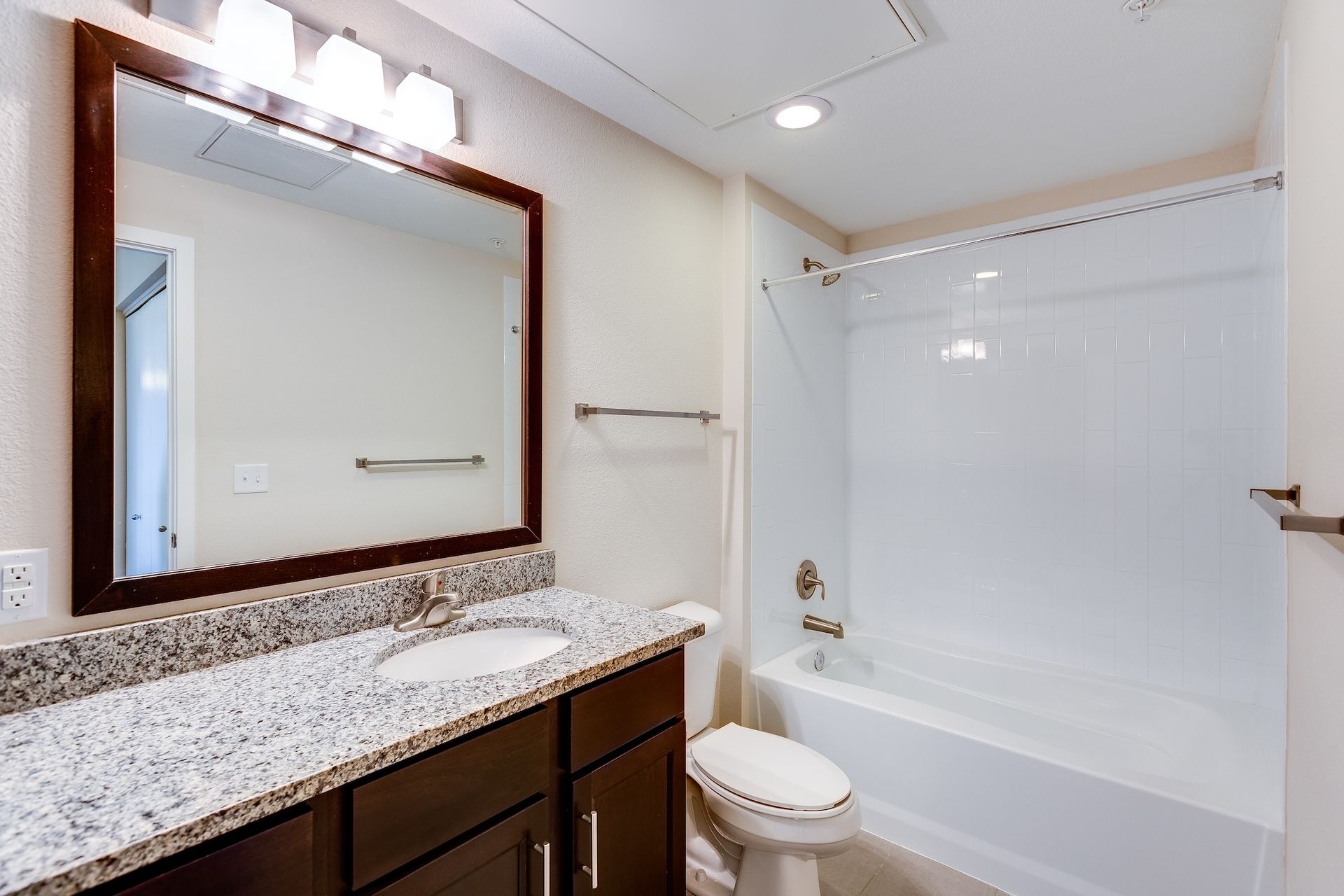 Modern bathroom with granite vanity, large mirror, and white tub-shower combo