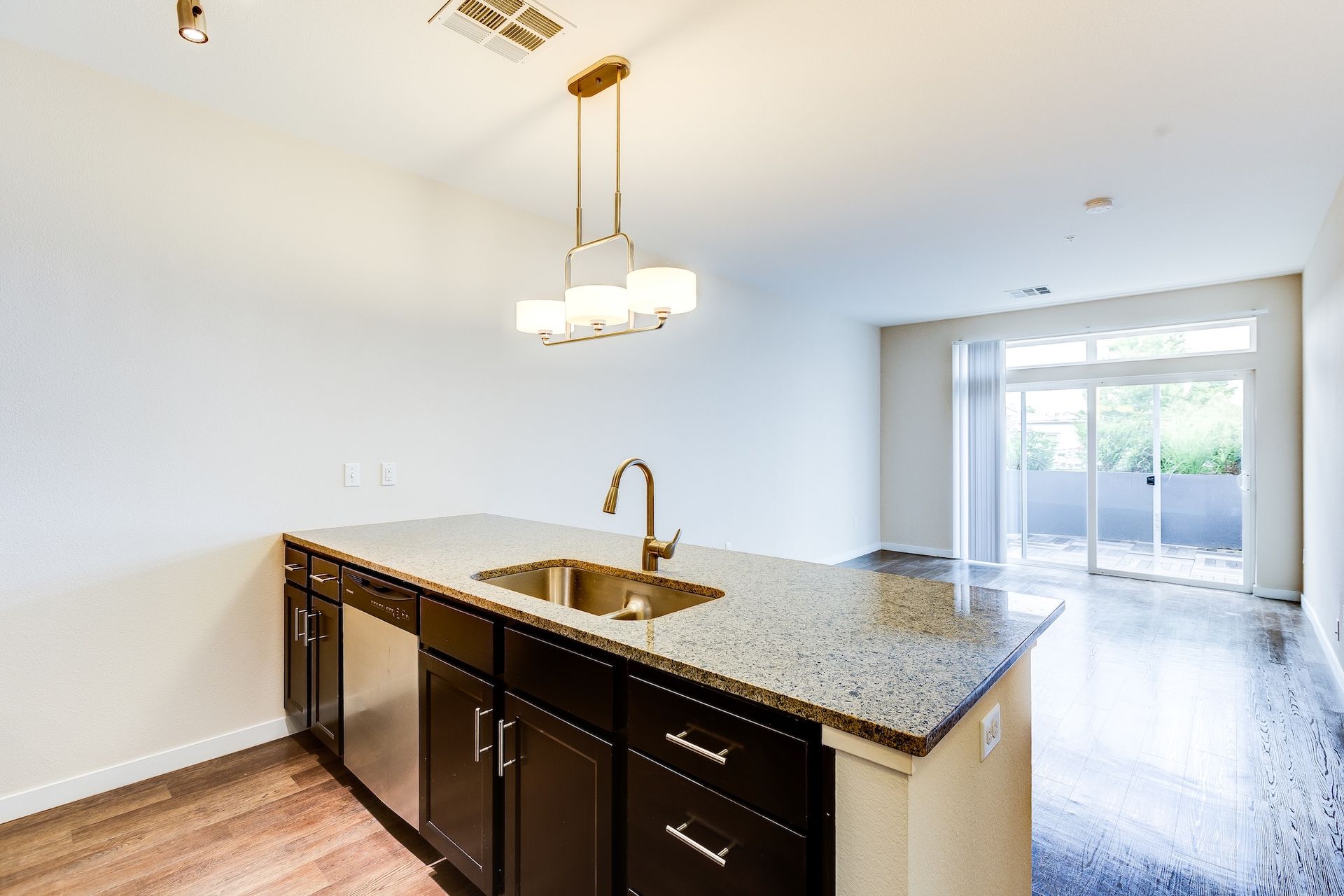 Empty modern kitchen with granite island, dark cabinets, pendant lights, and sliding glass doors to patio.