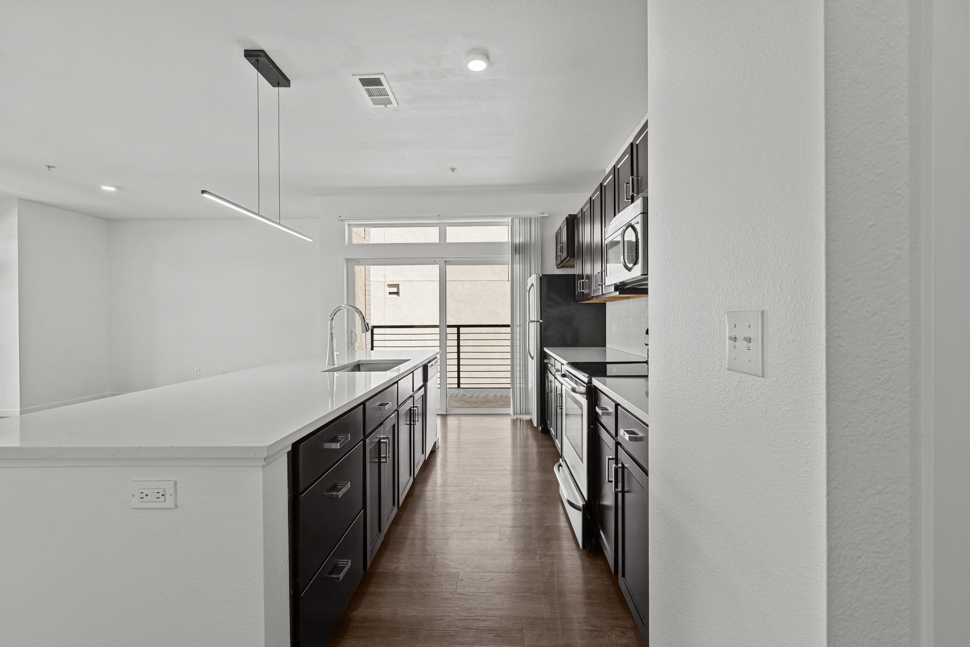 Modern white kitchen with dark cabinets, island, wood floor, and bright windows.