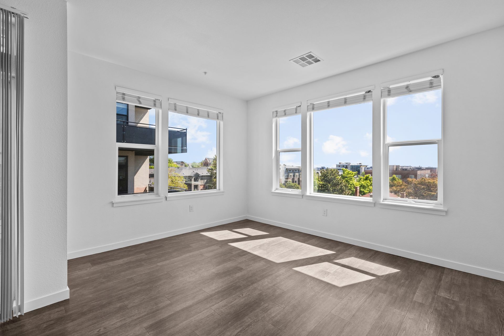 Bright empty room with large windows, white walls, and wood flooring, sunlight casting window shadows