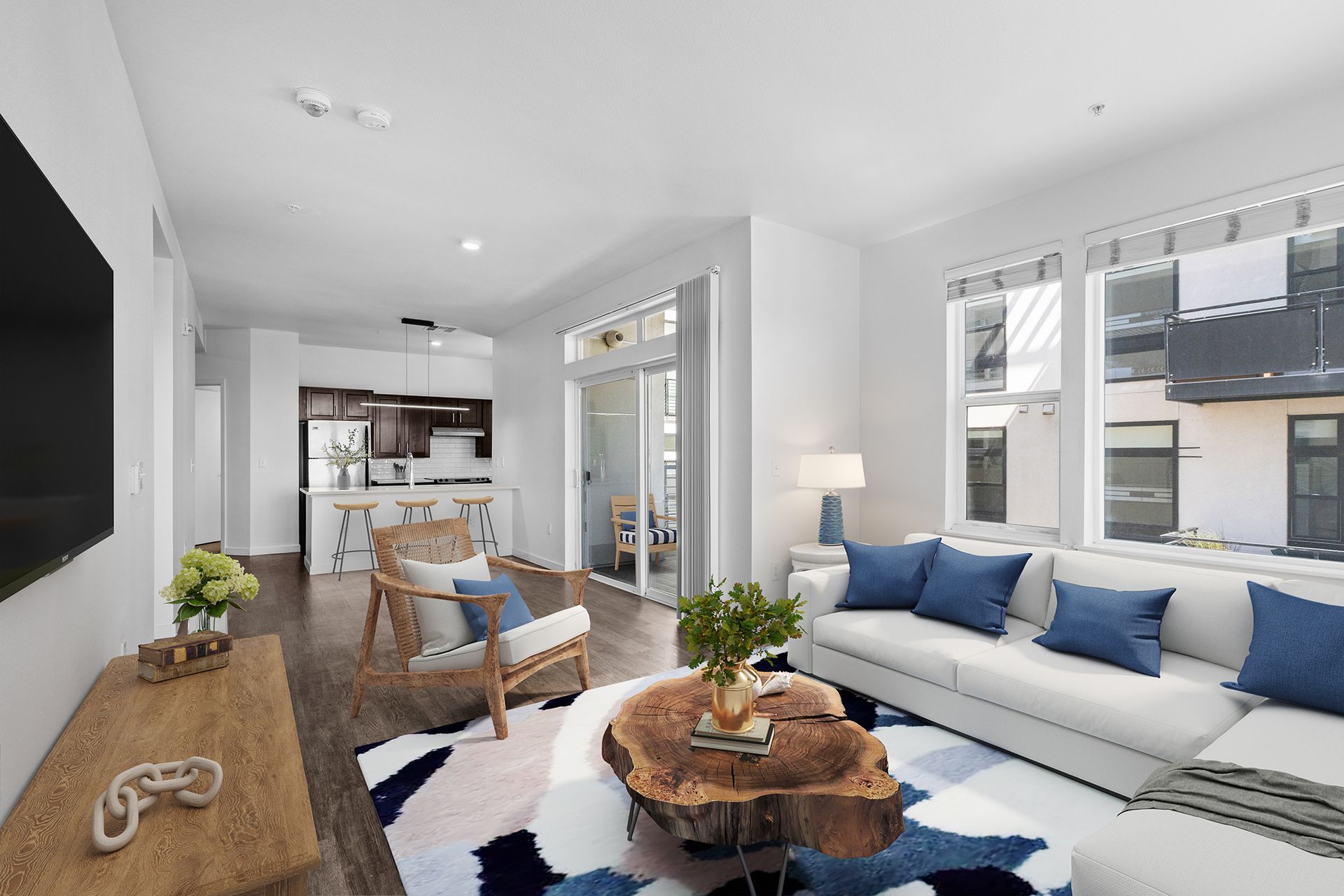 Bright modern living room with white sectional, blue accents, coffee table, and open kitchen beyond
