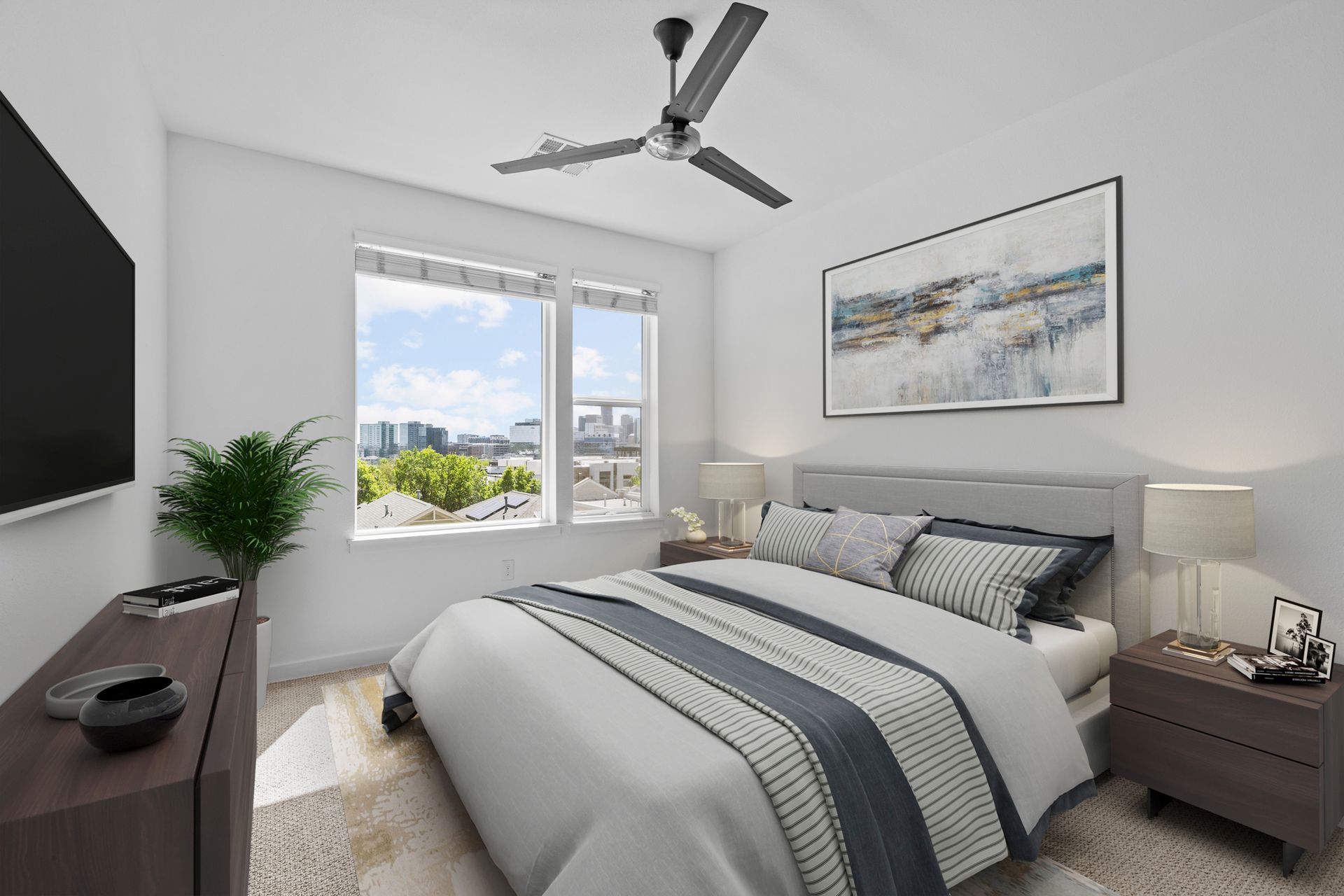 Bright bedroom with gray bed, ceiling fan, nightstand lamps, and a city view through a window.