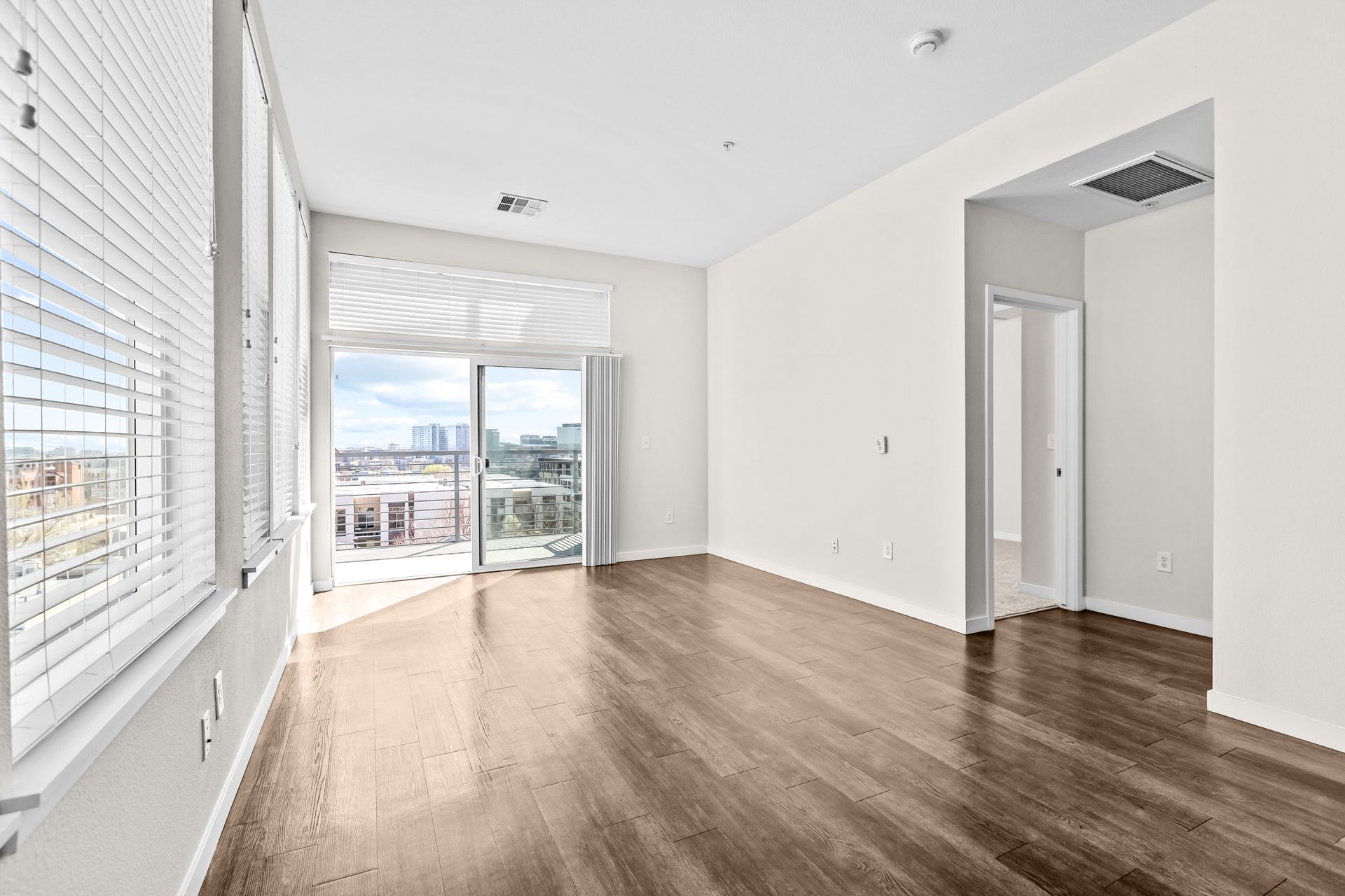 Empty modern apartment living room with wood floors, large windows, and balcony doors.