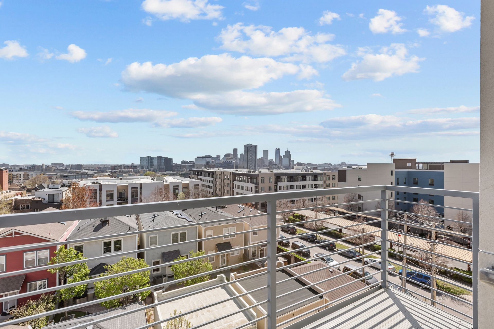 City skyline view from a balcony with metal railing under a bright blue sky with clouds