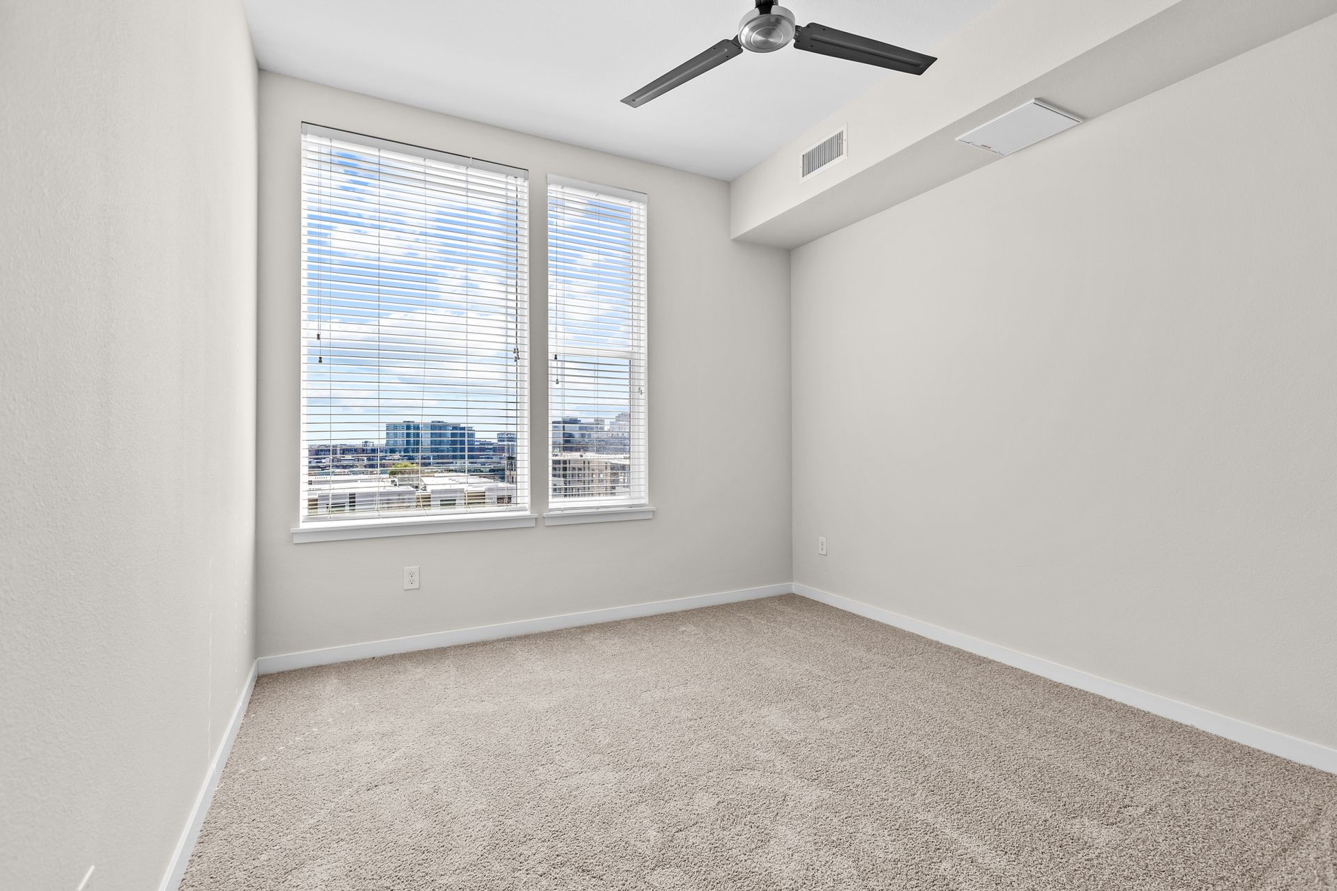 Empty carpeted bedroom with large window, white walls, and ceiling fan