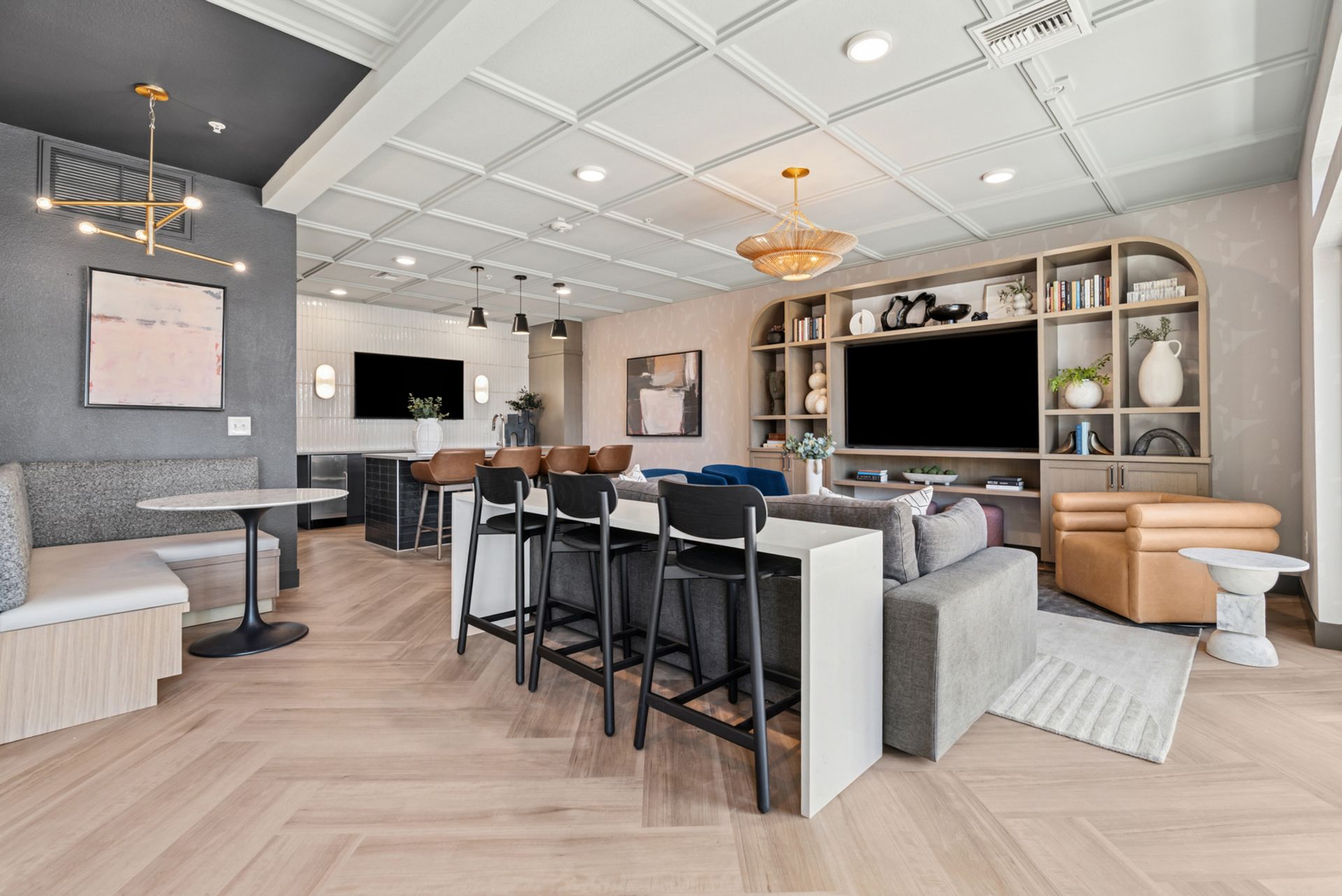 Modern lounge with bar seating, large TV, gray sofas, tan chair, and light wood flooring