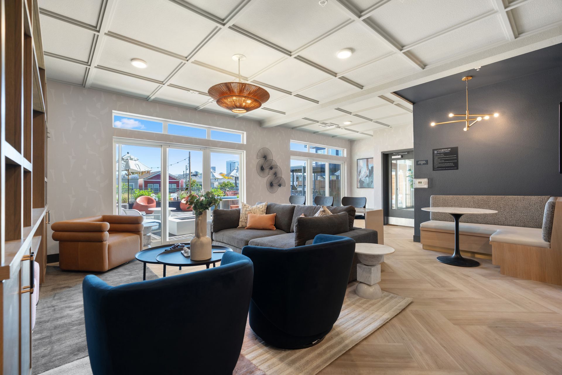 Modern lounge with black chairs, tan sofas, large windows, and a bar area under a patterned ceiling