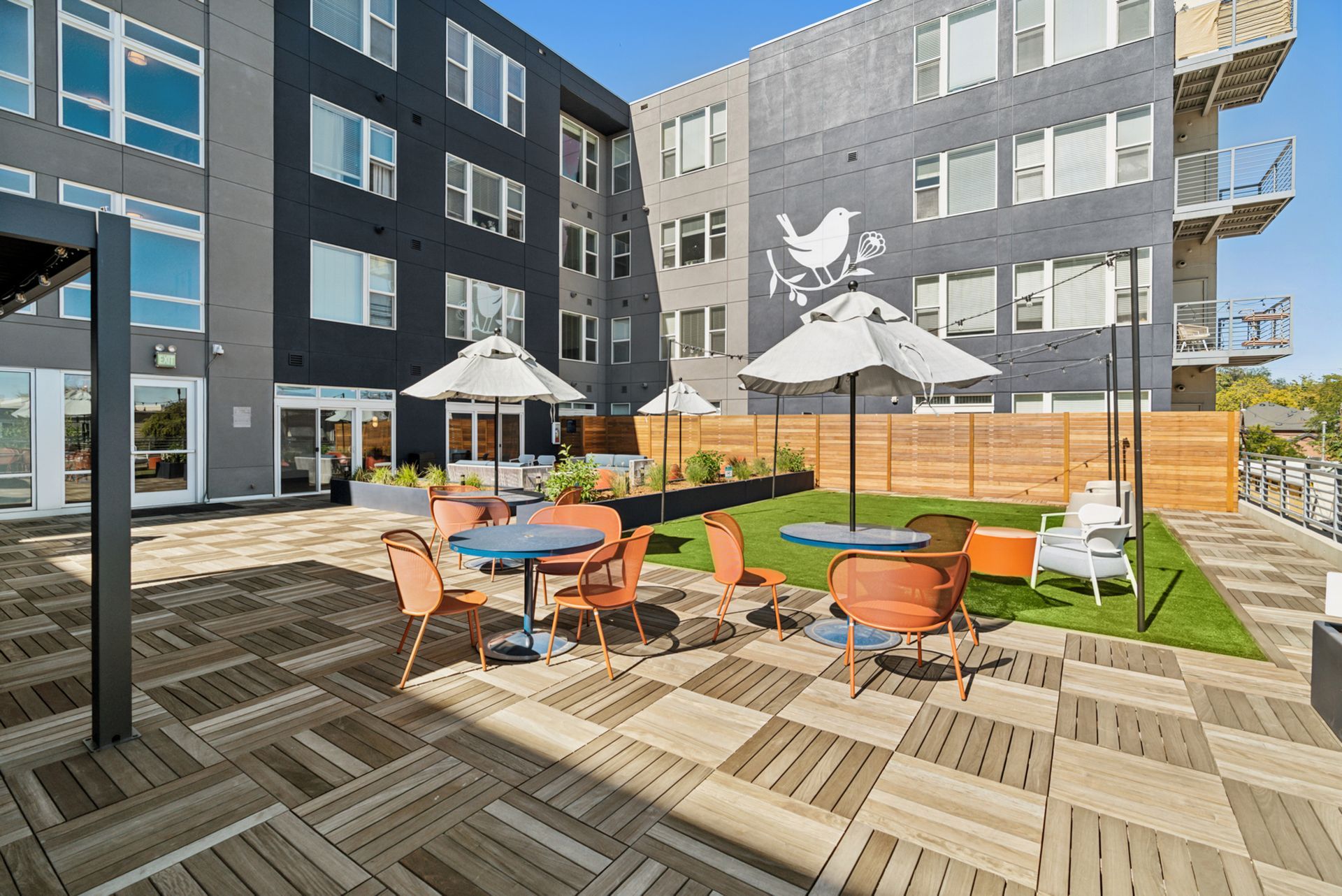 Modern apartment courtyard with patio seating, umbrellas, and raised wooden planters