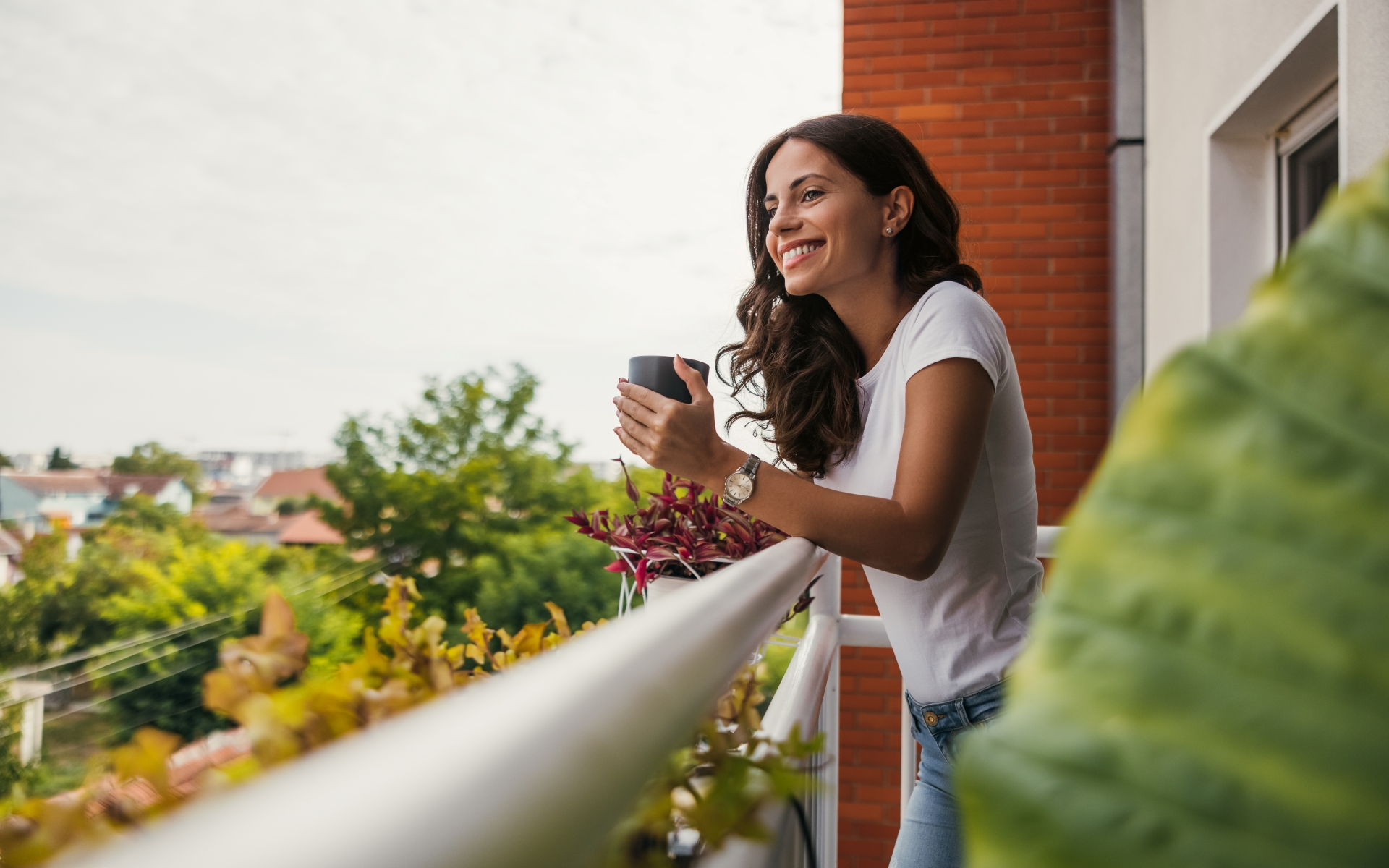A woman is standing on a balcony holding a cup of coffee.