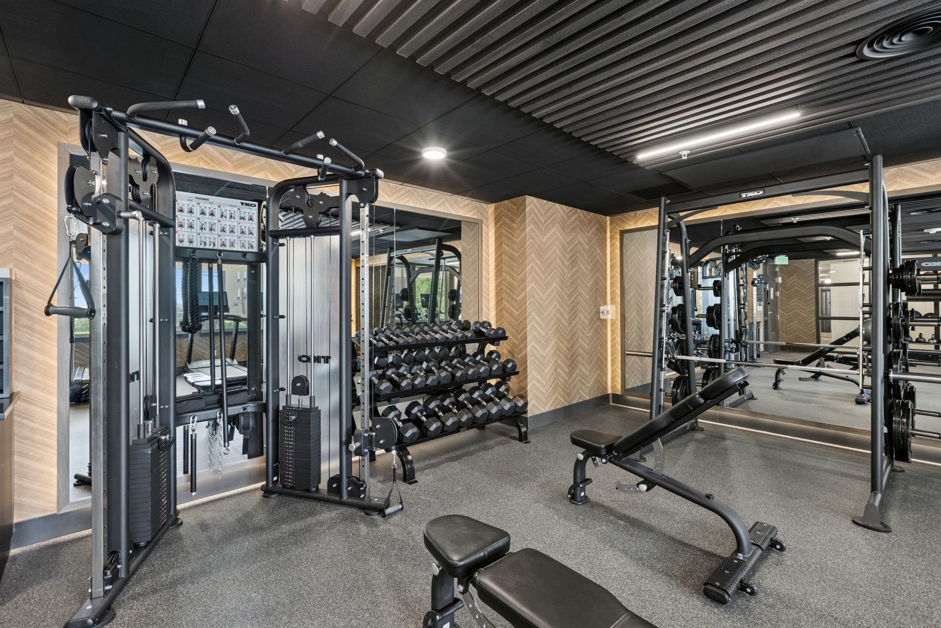 Modern gym interior with cable machines, dumbbell rack, bench, and rubber flooring