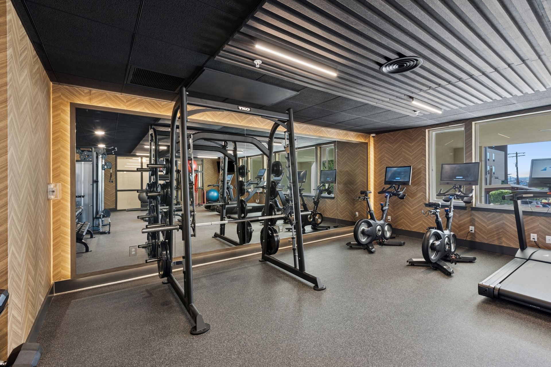 Gym with weight rack, exercise bikes, treadmill, and large mirror reflecting equipment.