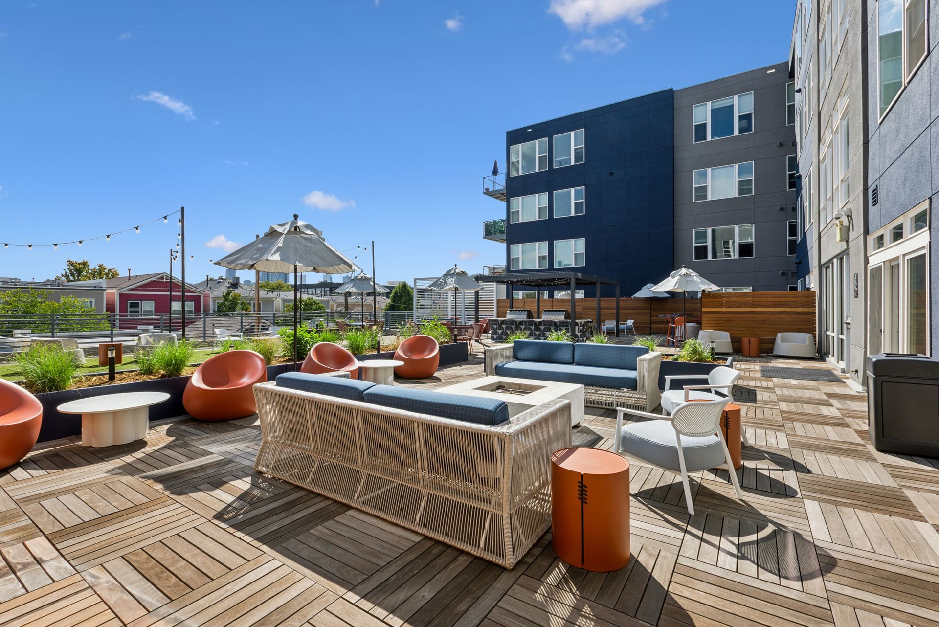 Modern rooftop terrace with seating, orange planters, and city buildings under a blue sky