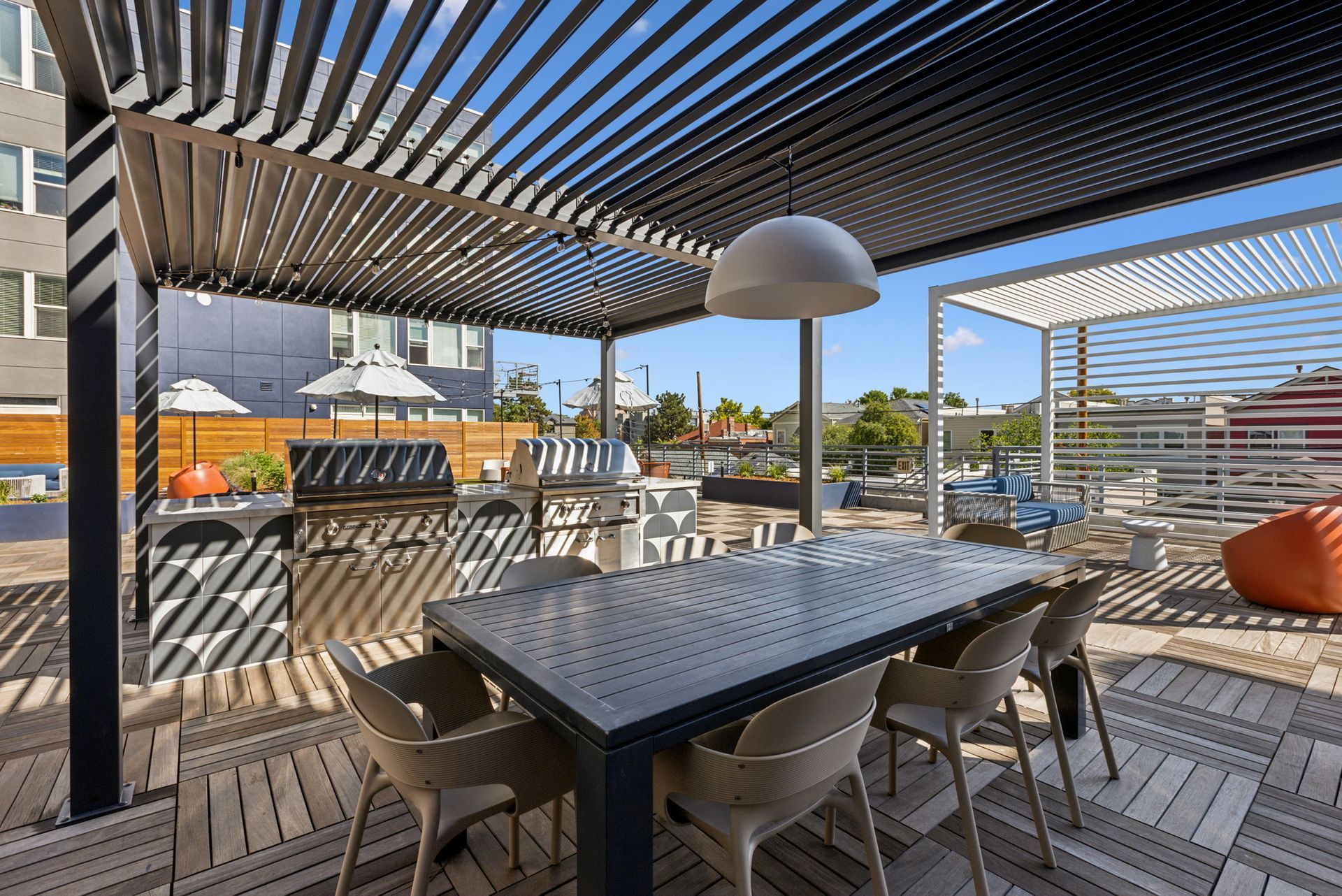 Outdoor patio dining area with black table, chairs, pergola shade, and city view