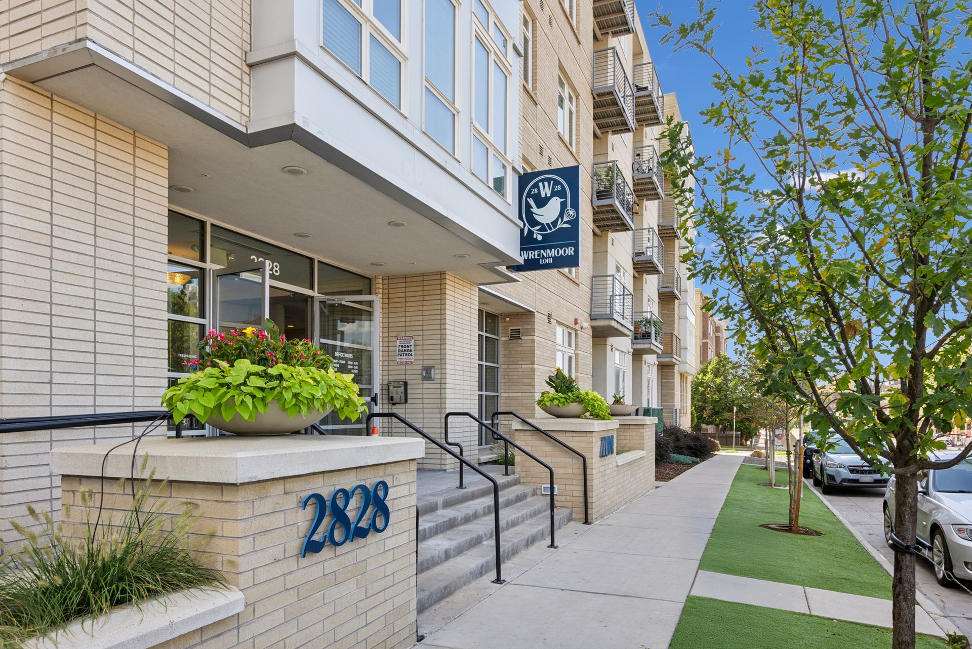 Apartment building entrance with stairs, planter, and sidewalk on a sunny street